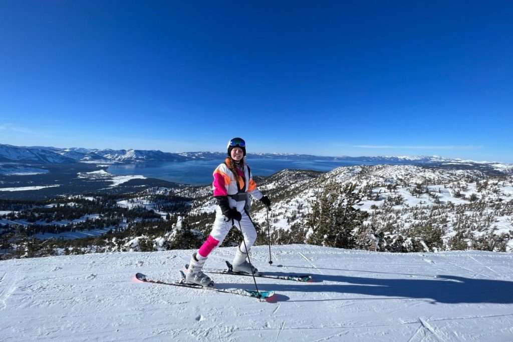 Traveler Liz skiing at Heavenly Mountain Resort with a panoramic view of snow-covered mountains and Lake Tahoe in winter.