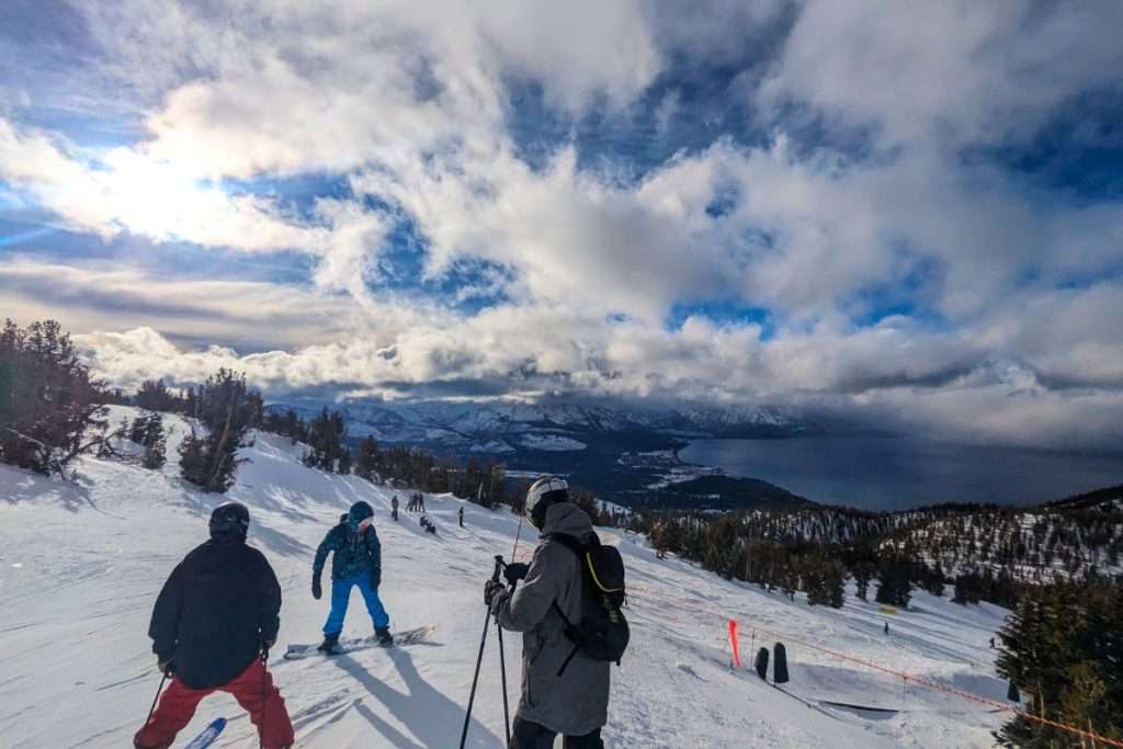 Skiers and snowboarders on a snowy mountain slope in South Lake Tahoe with dramatic winter clouds over Lake Tahoe