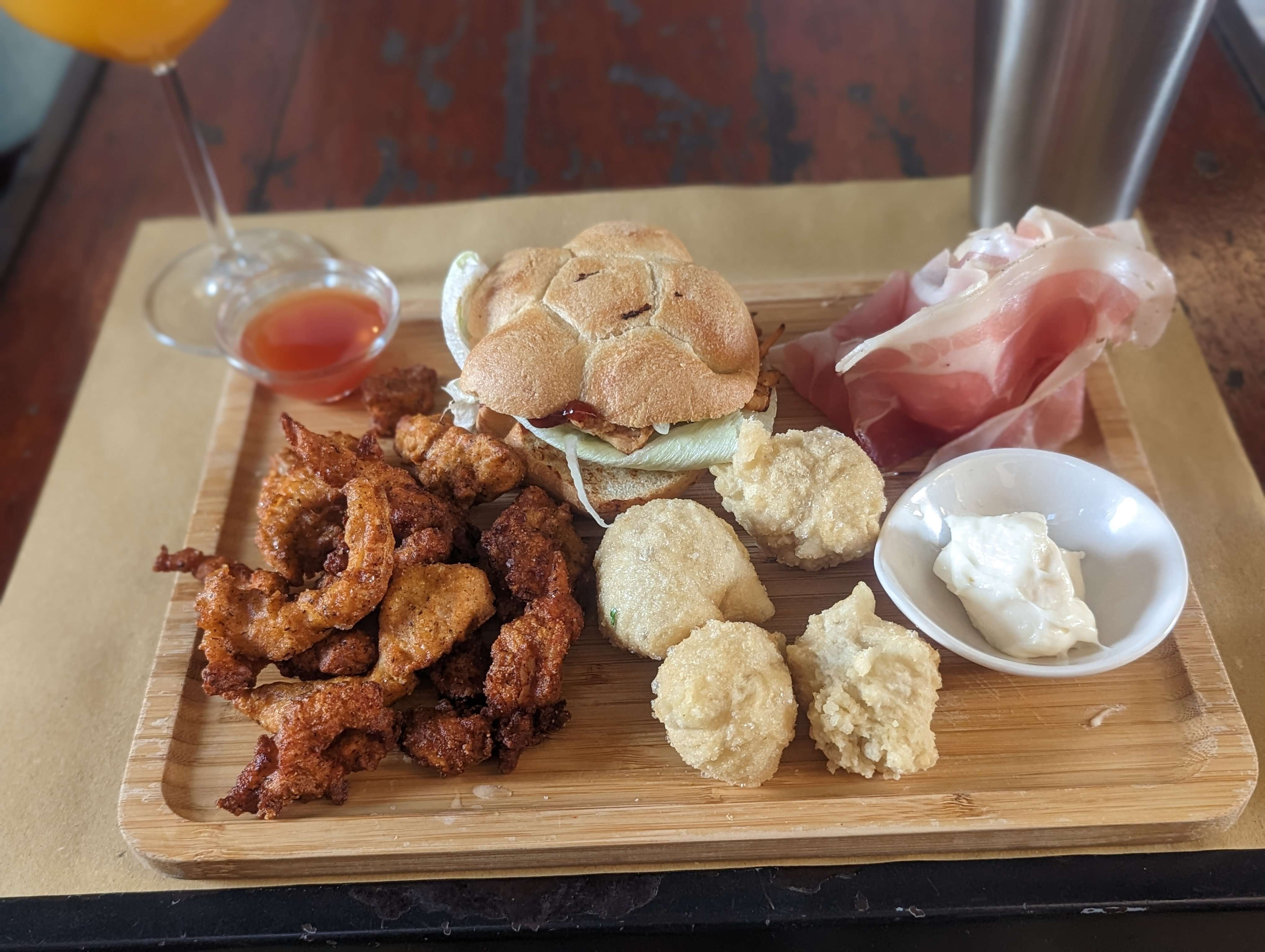 A wooden tray with 3 different types of bite-size food alongside my drink at a bar in Florence, Italy.
