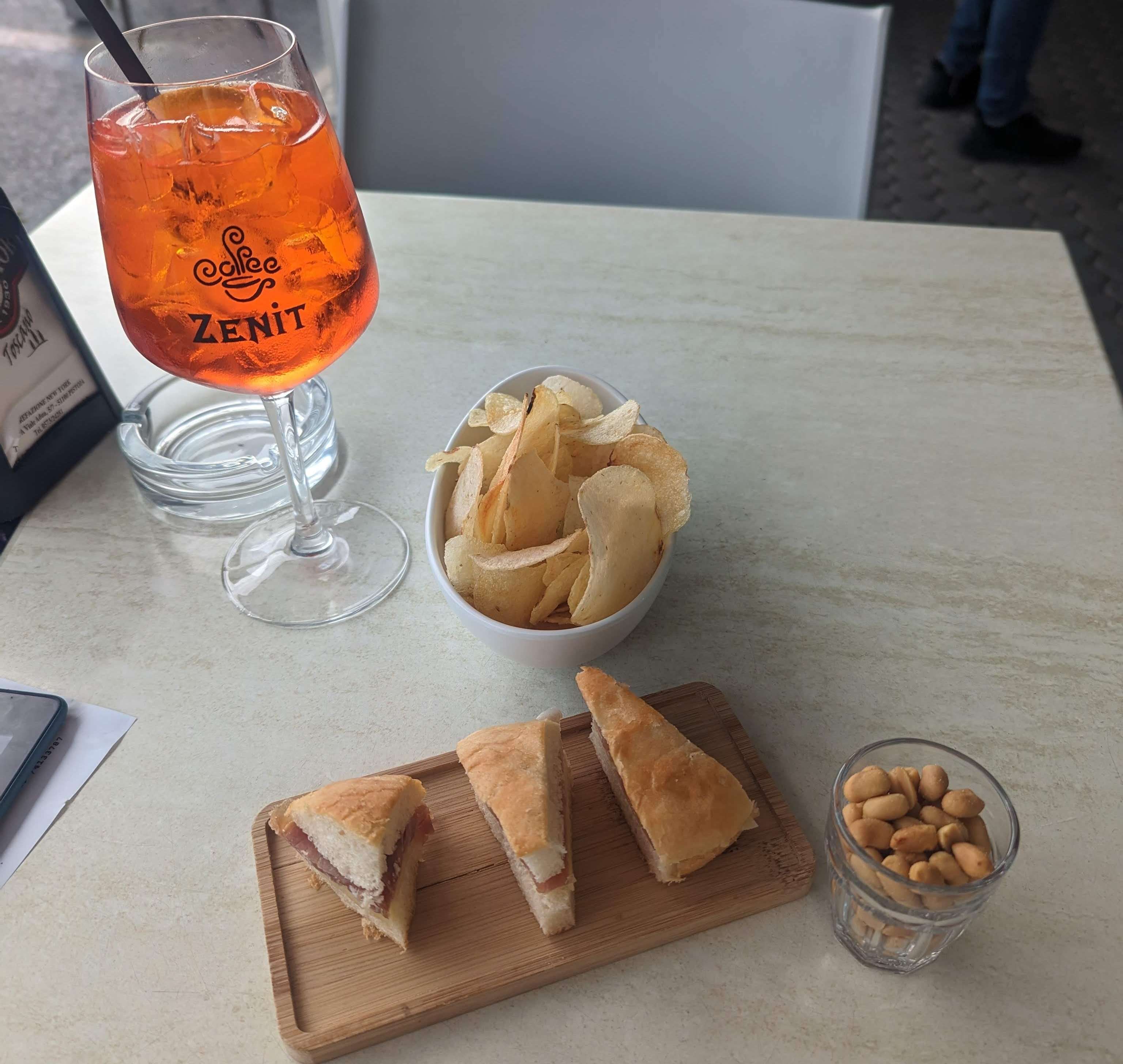 Little finger sandwiches, chips, and peanuts next to my Aperitivo drink at a bar in Italy.