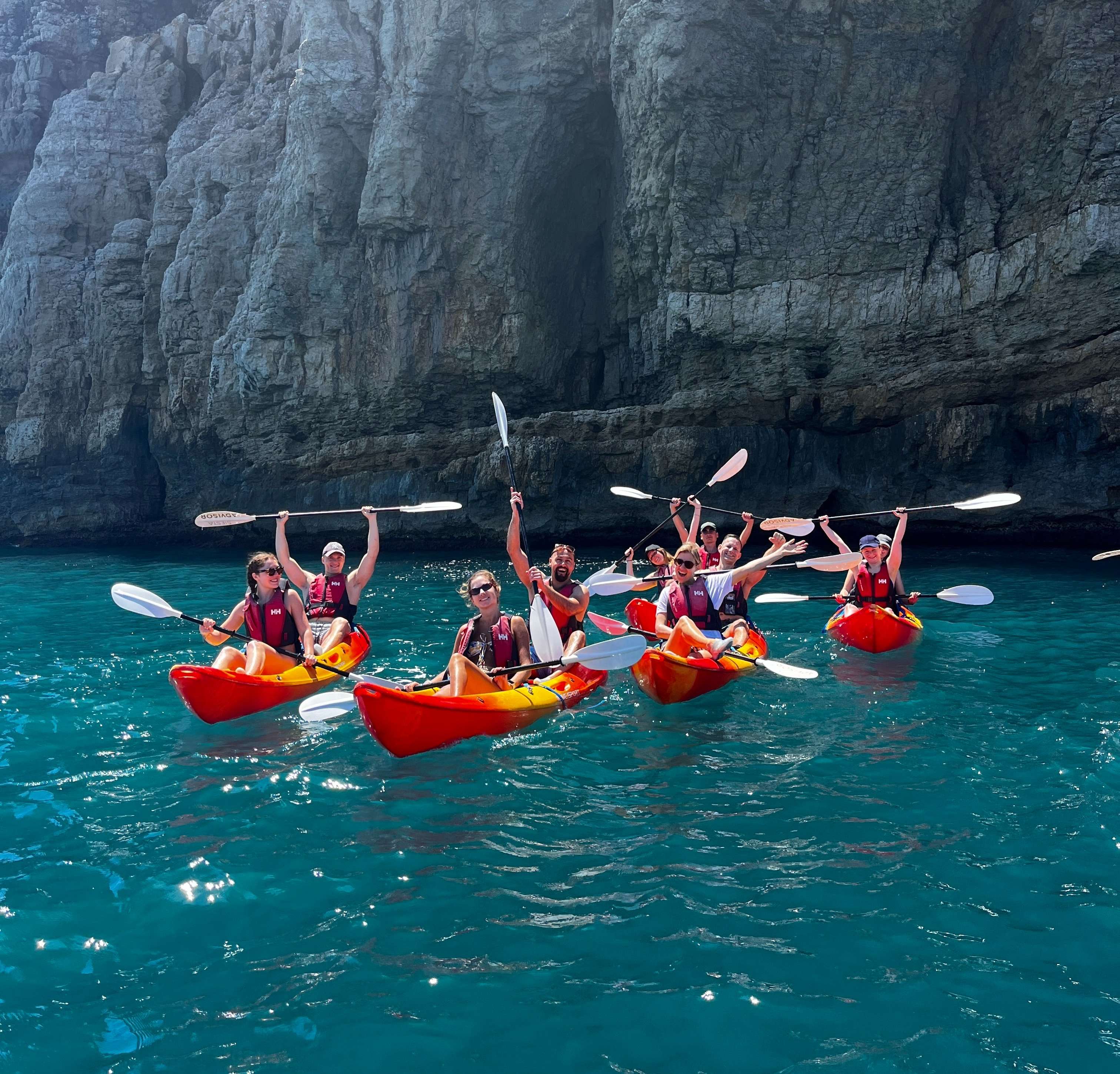 A group of friends holding up their paddles while sitting in their kayaks.
