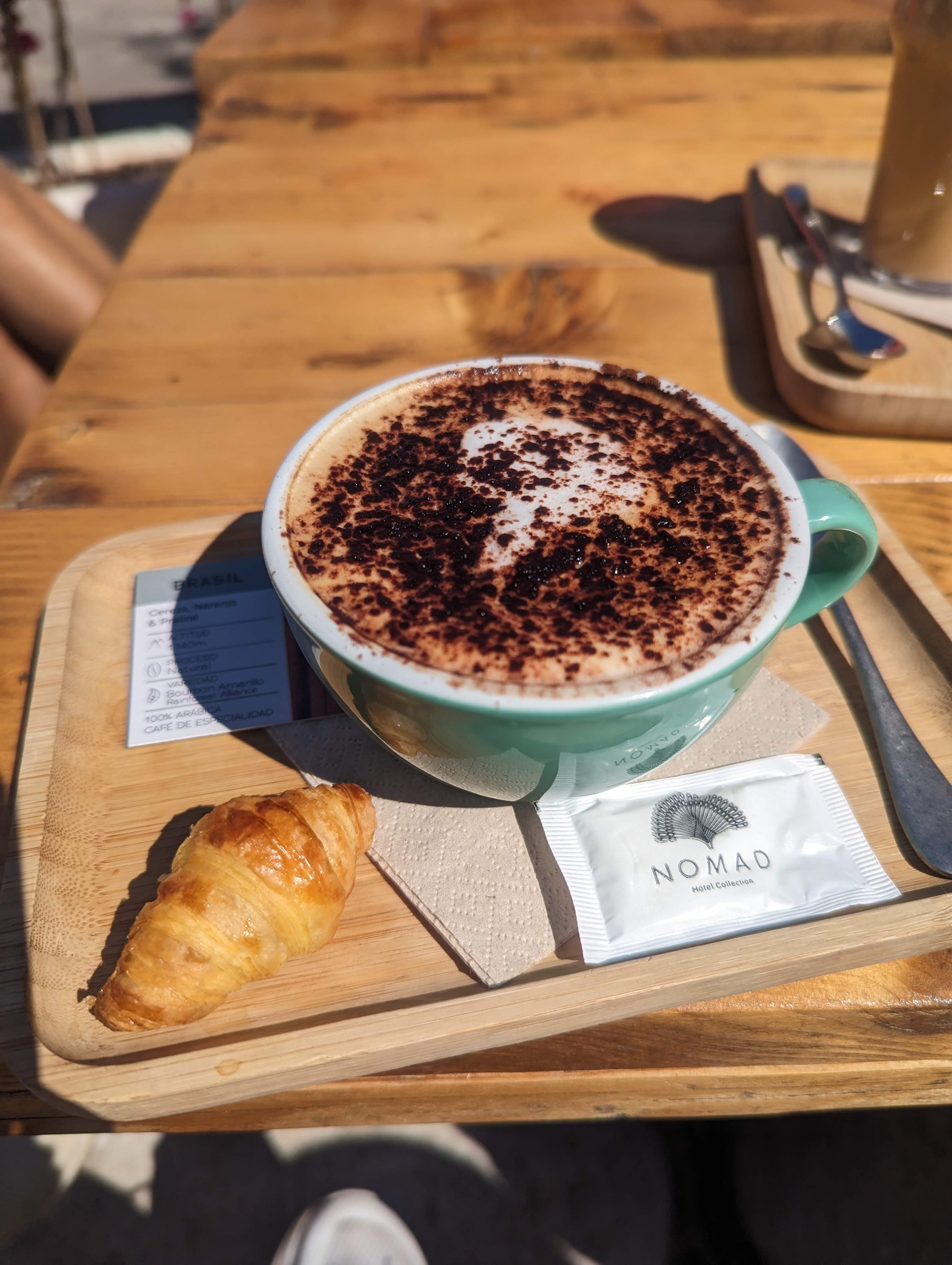 A beautiful cappuccino with a miniature croissant next to it.