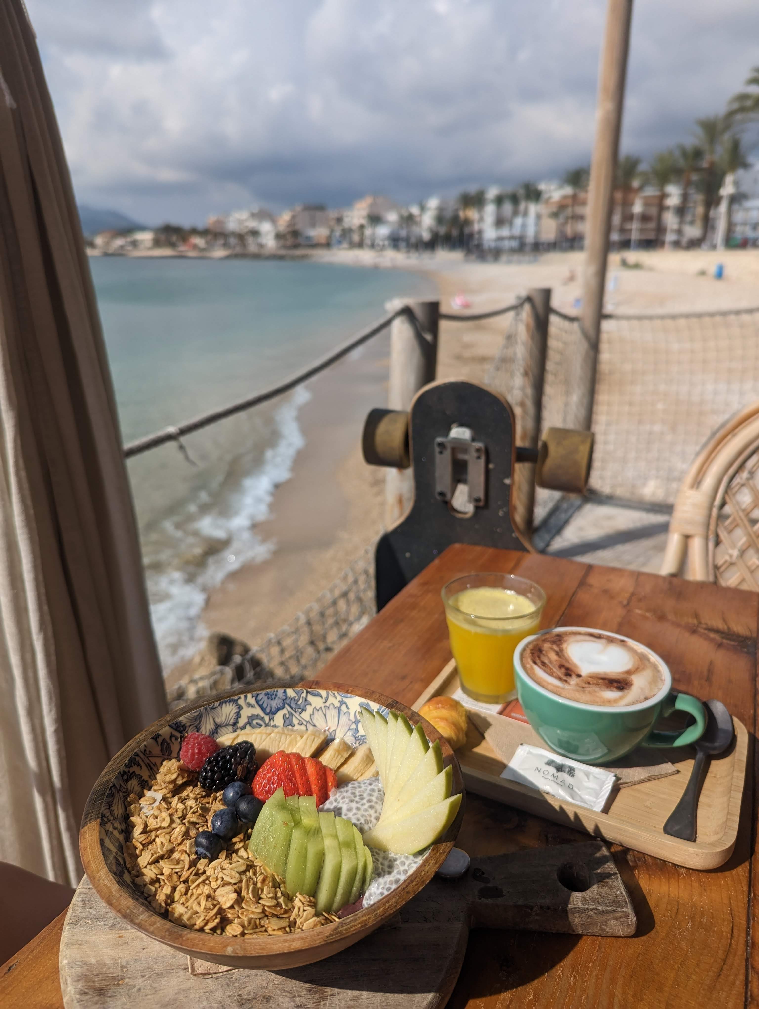 A view of breakfast in front of the water, consisting of an acai bowl and capuccino.