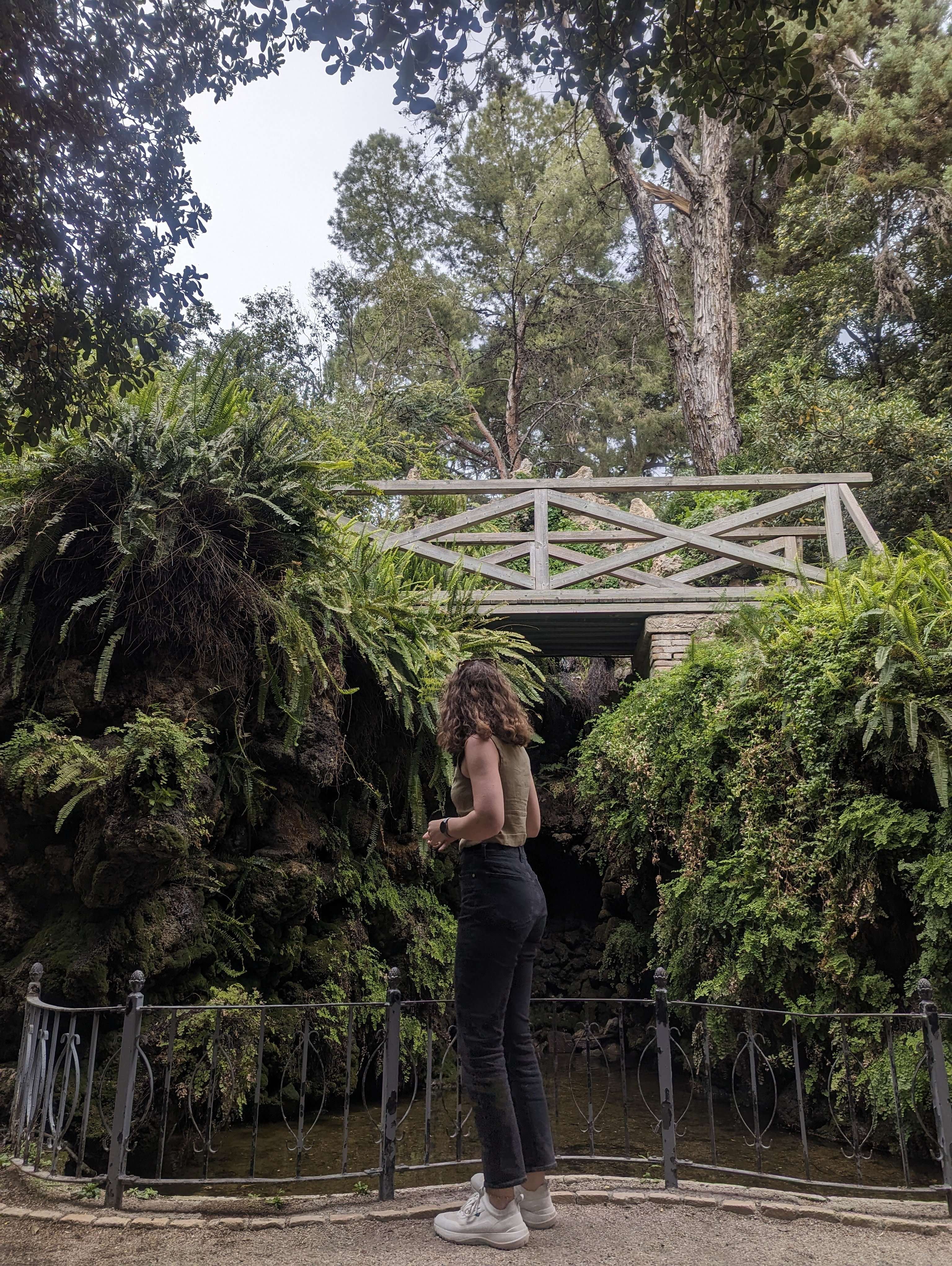 Me (Traveler Liz) in Jardi de Montfort standing in front of a bridge, surrounded by greenery.