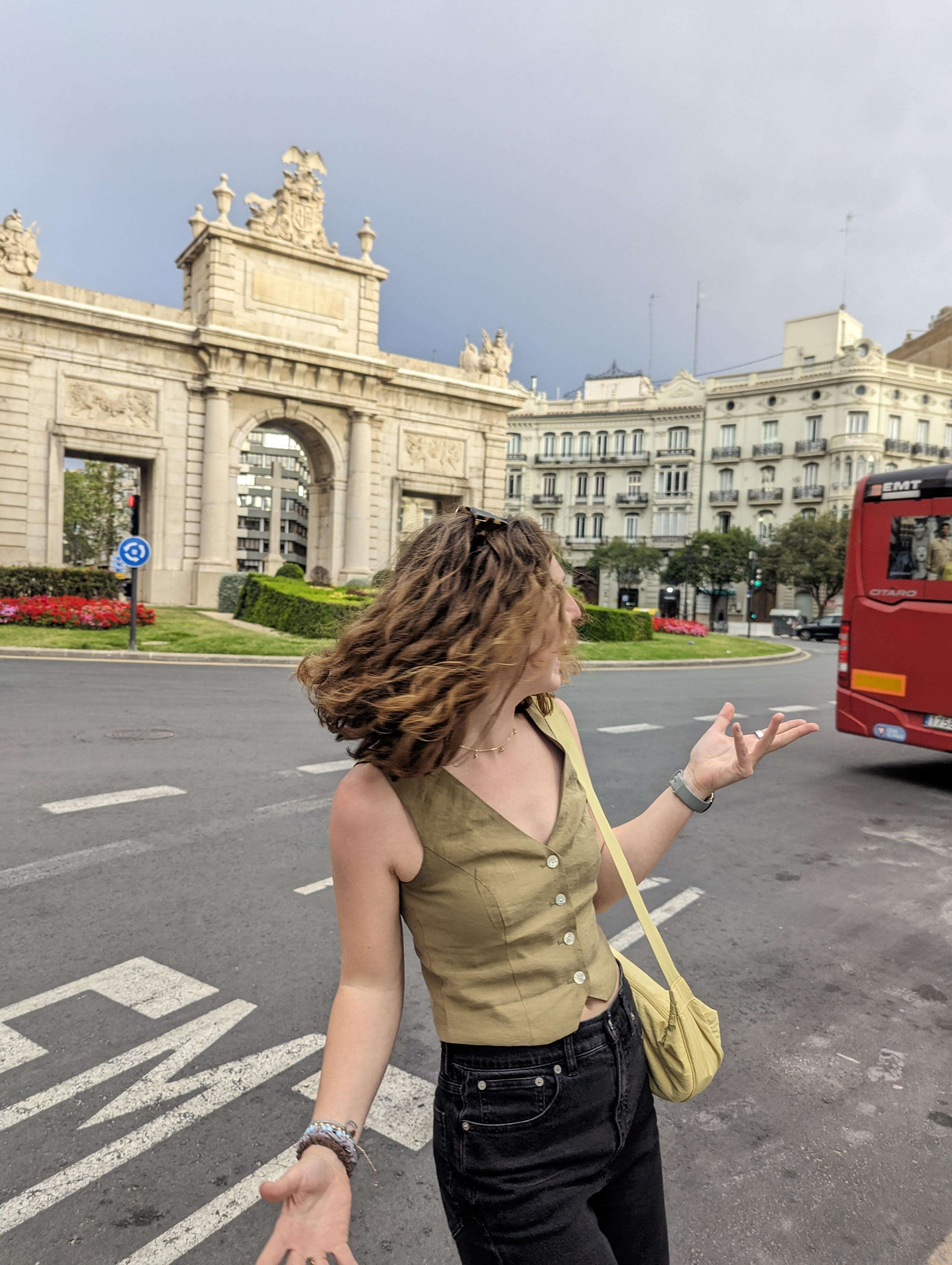 Me (Traveler Liz) confused in front of a road in Valencia with a landmark behind me.