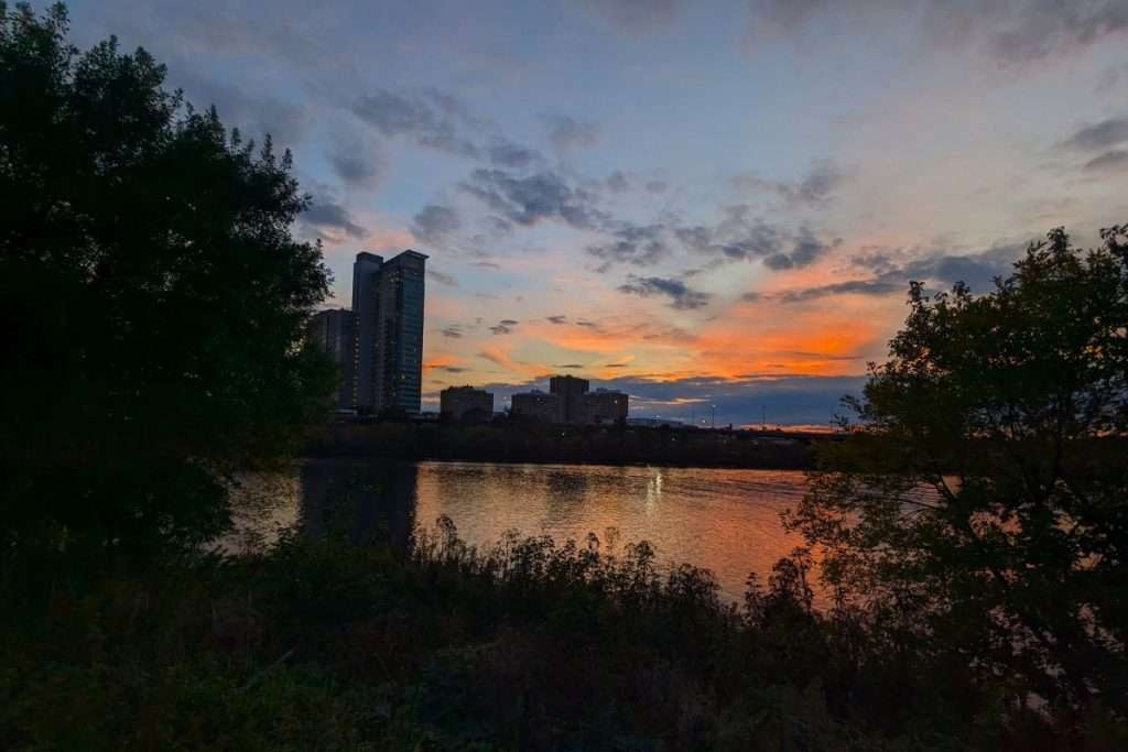 Sunset reflecting on the Charles River with Boston high-rise buildings and trees in the foreground.