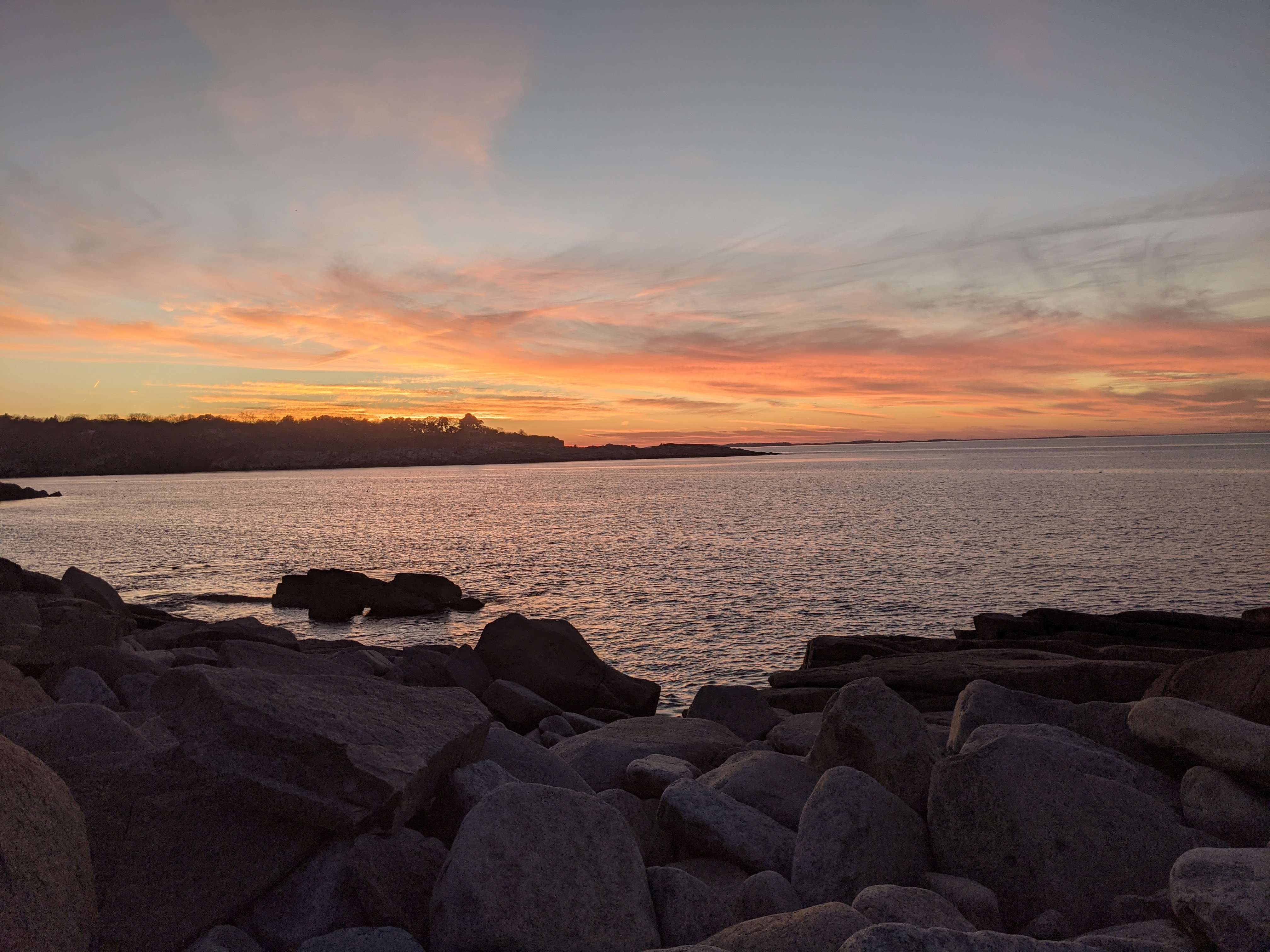 Lots of rocks in front of the lake with the sunset over the top.