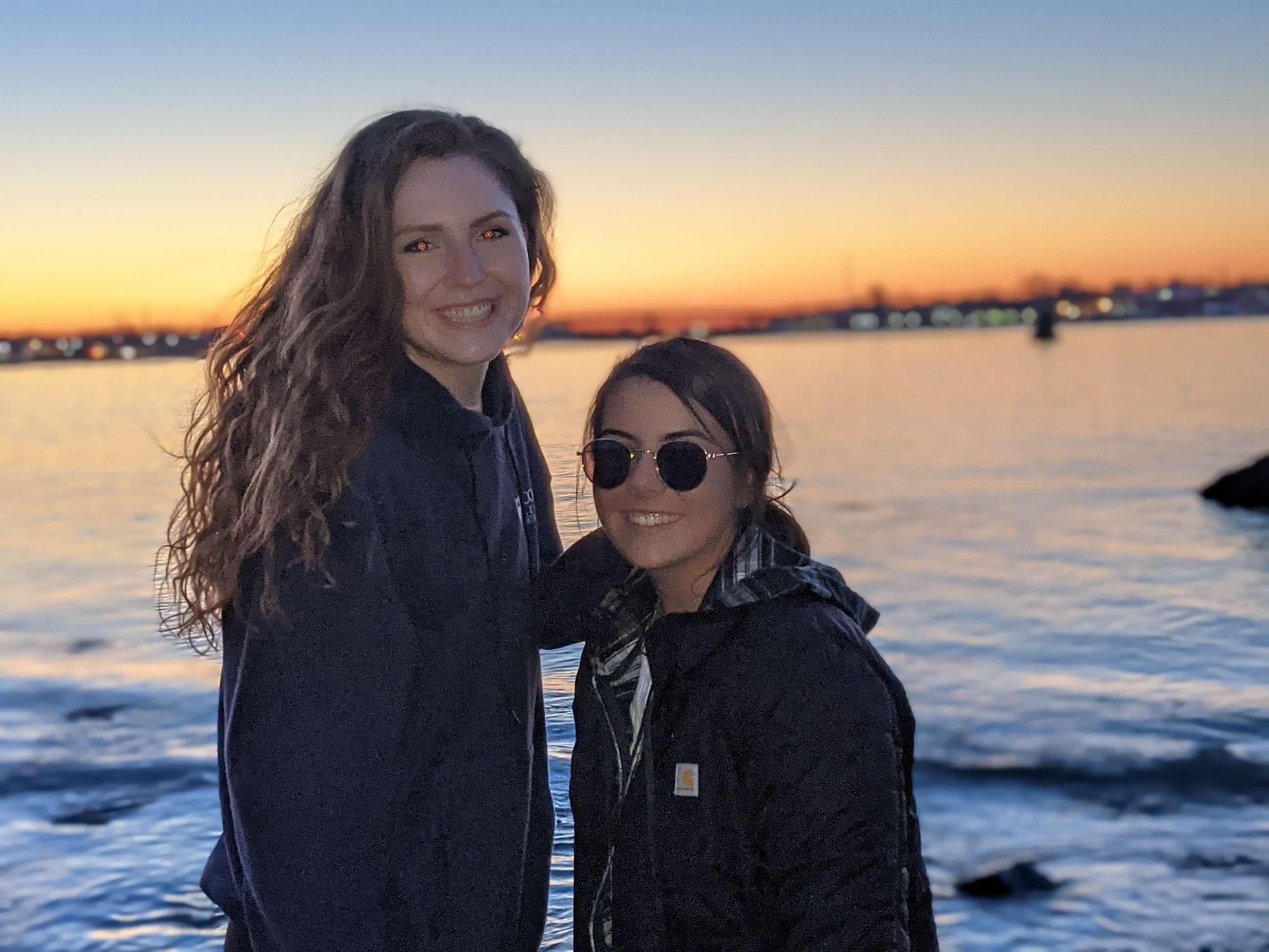 My friend and I (Traveler Liz) posing in front of the sunset with water behind us.