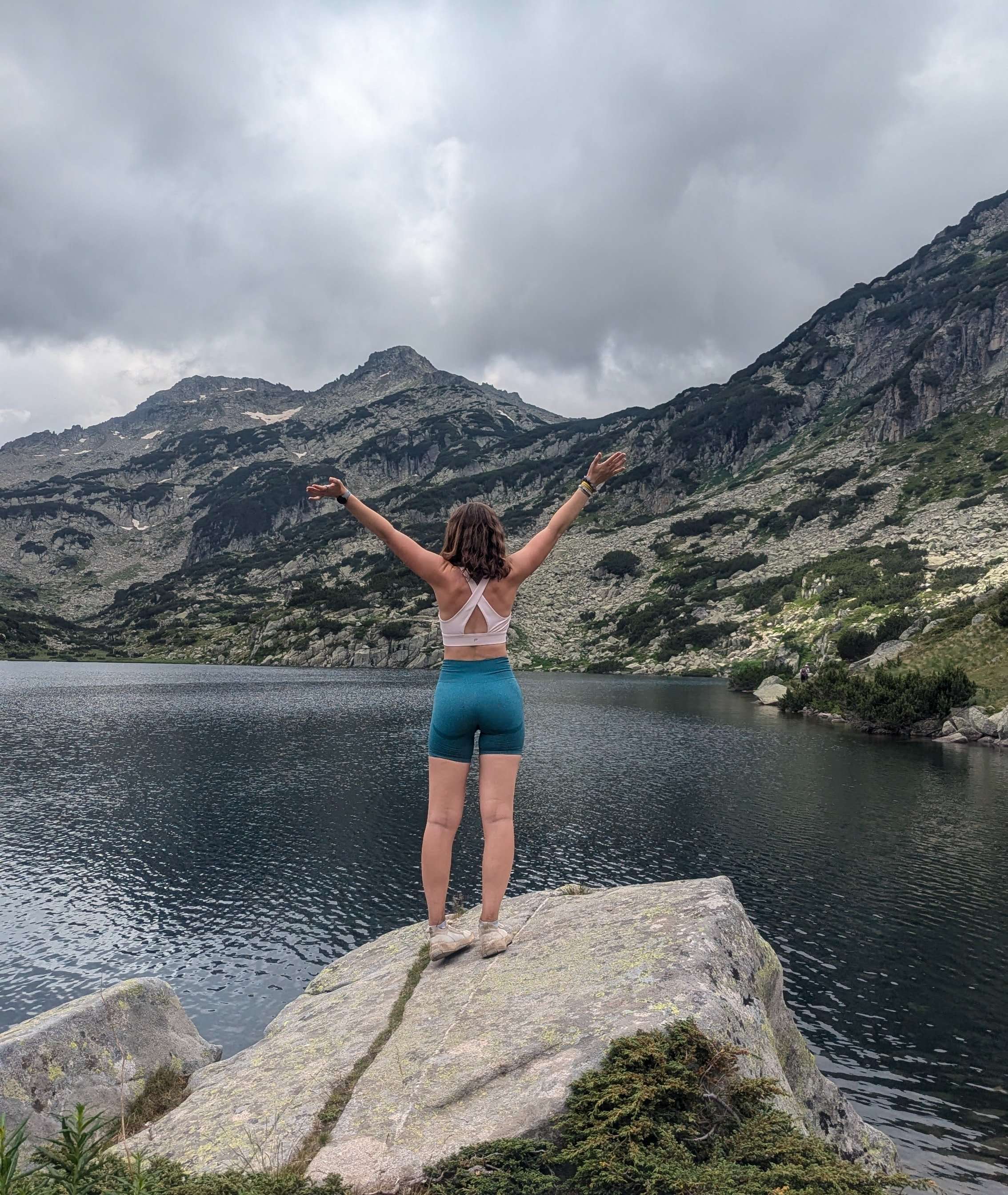 Me (Traveler Liz) with my arms raised overlooking a lake with the Bulgarian mountains in the back.