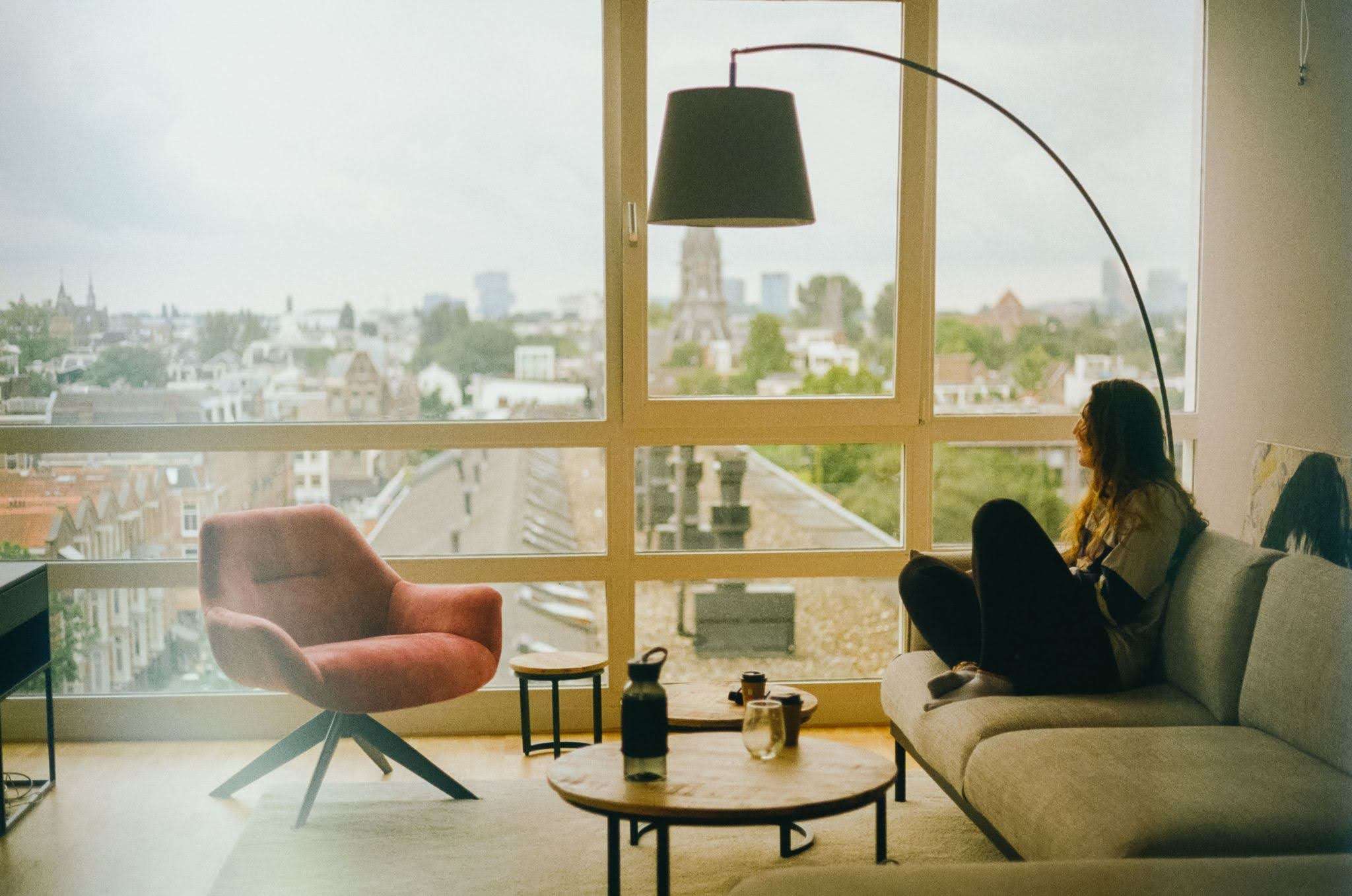 Me (Budget Traveler Liz) sitting in front of the window in Amsterdam with a gloomy haze to show off how I felt and looked when sick while traveling.