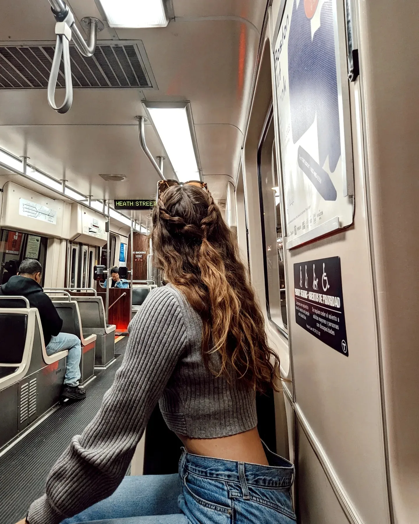 Me (Budget Traveler Liz) sitting on the train in Boston staring backwards at the people wearing Blue Jeans and a cropped gray sweater.