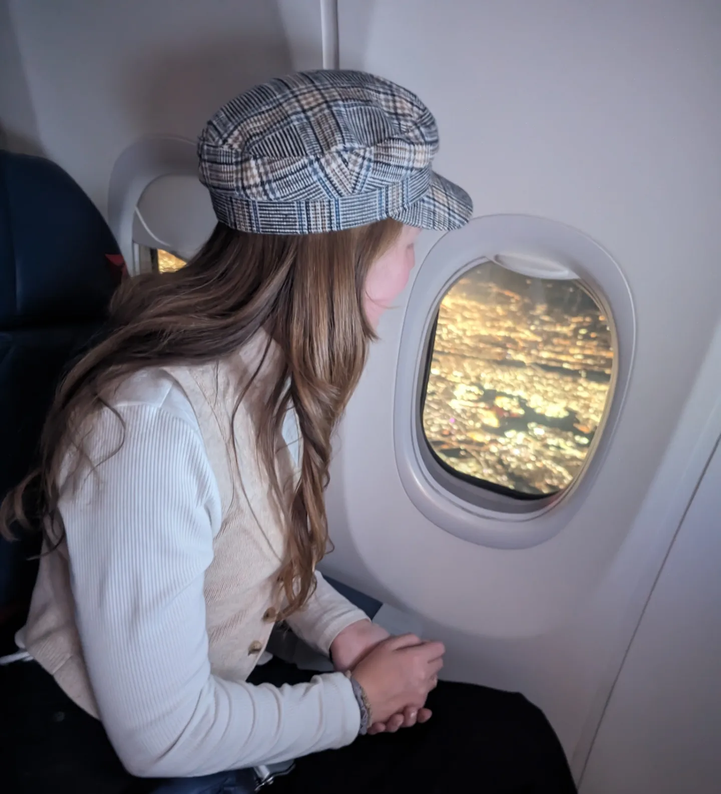 Me (Budget Traveler Liz) looking out the airplane window at a city of lights below.