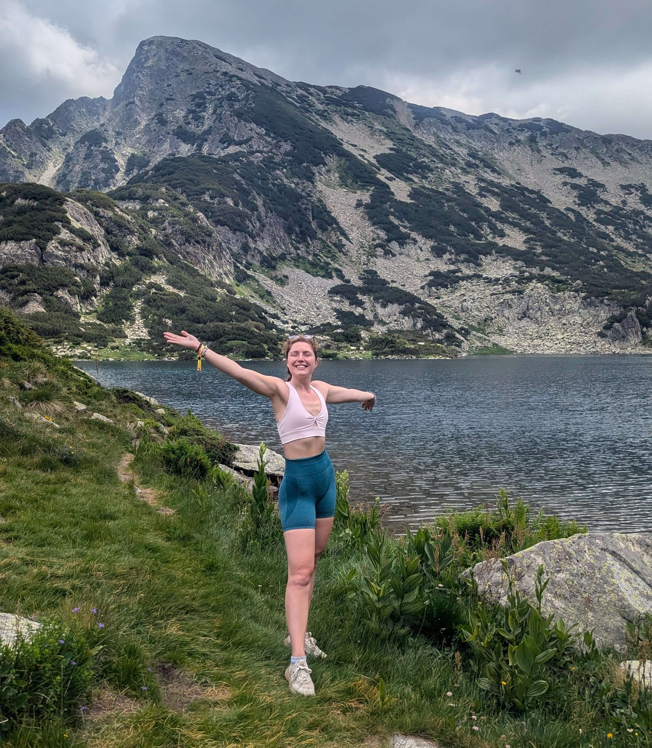 Me (Traveler Liz) standing with arms outspread in front of Bulgarian mountains while hiking.