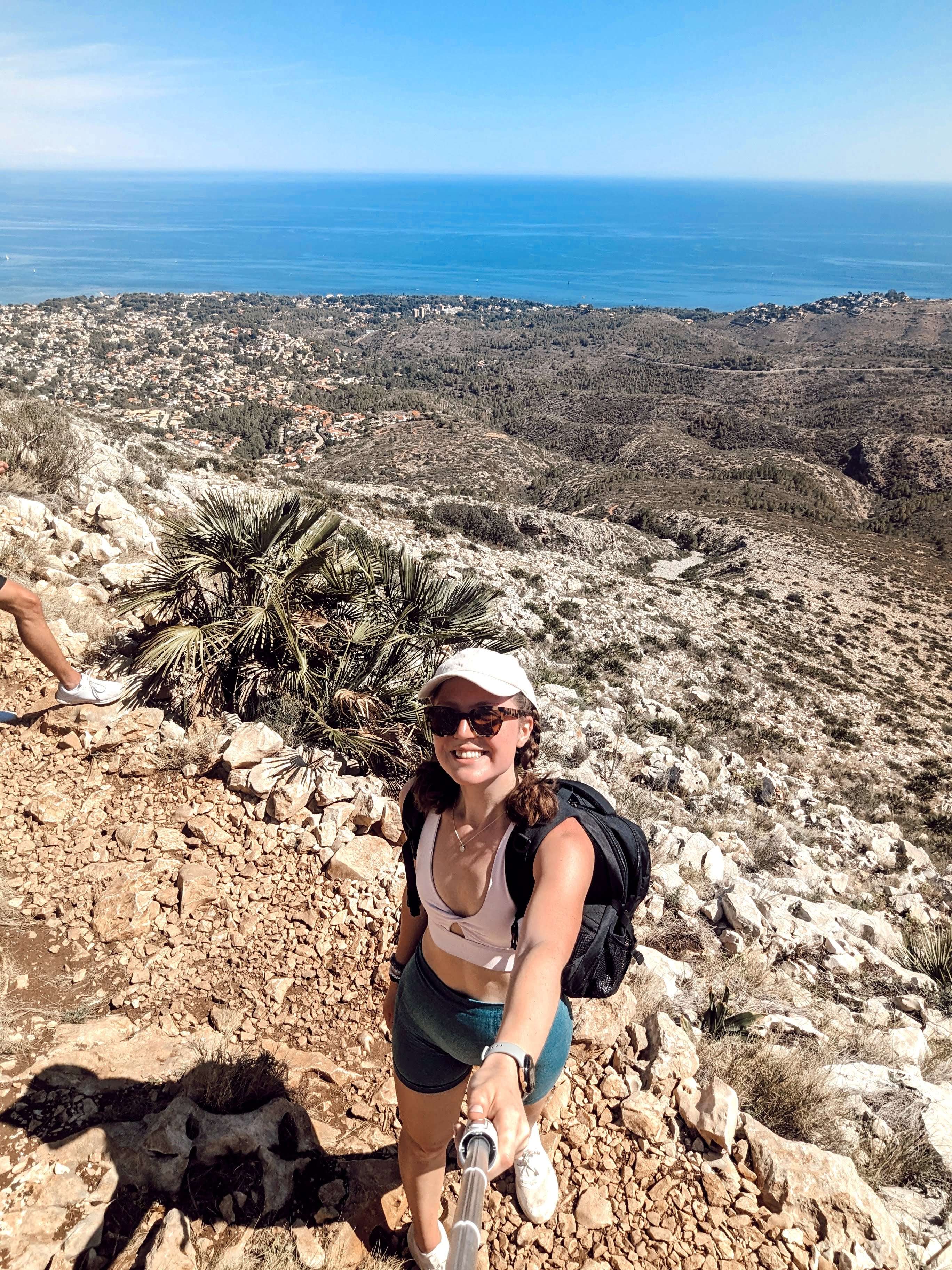 Me (Traveler Liz) standing at the top of a mountain I just hiked in Spain overlooking the ocean.