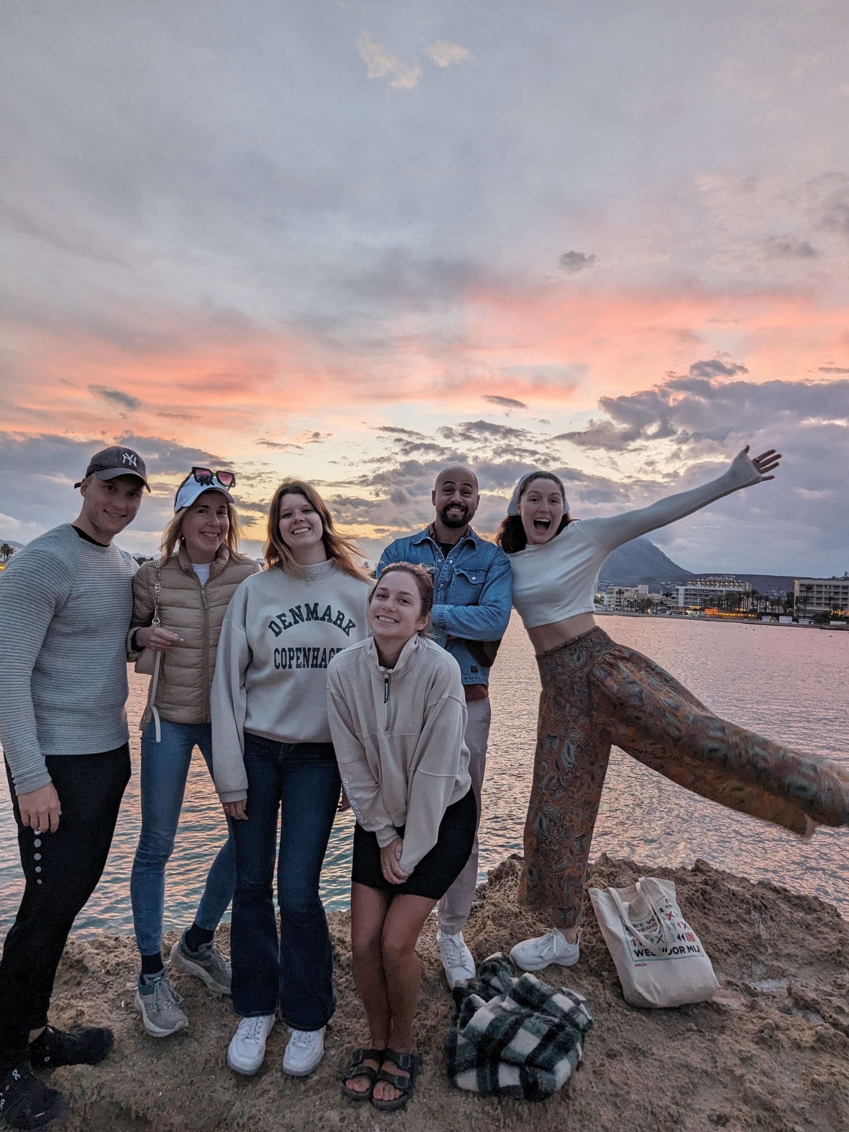 A group of friends standing on some rocks with the ocean and Montgo mountain behind us, and the sun setting in the background.