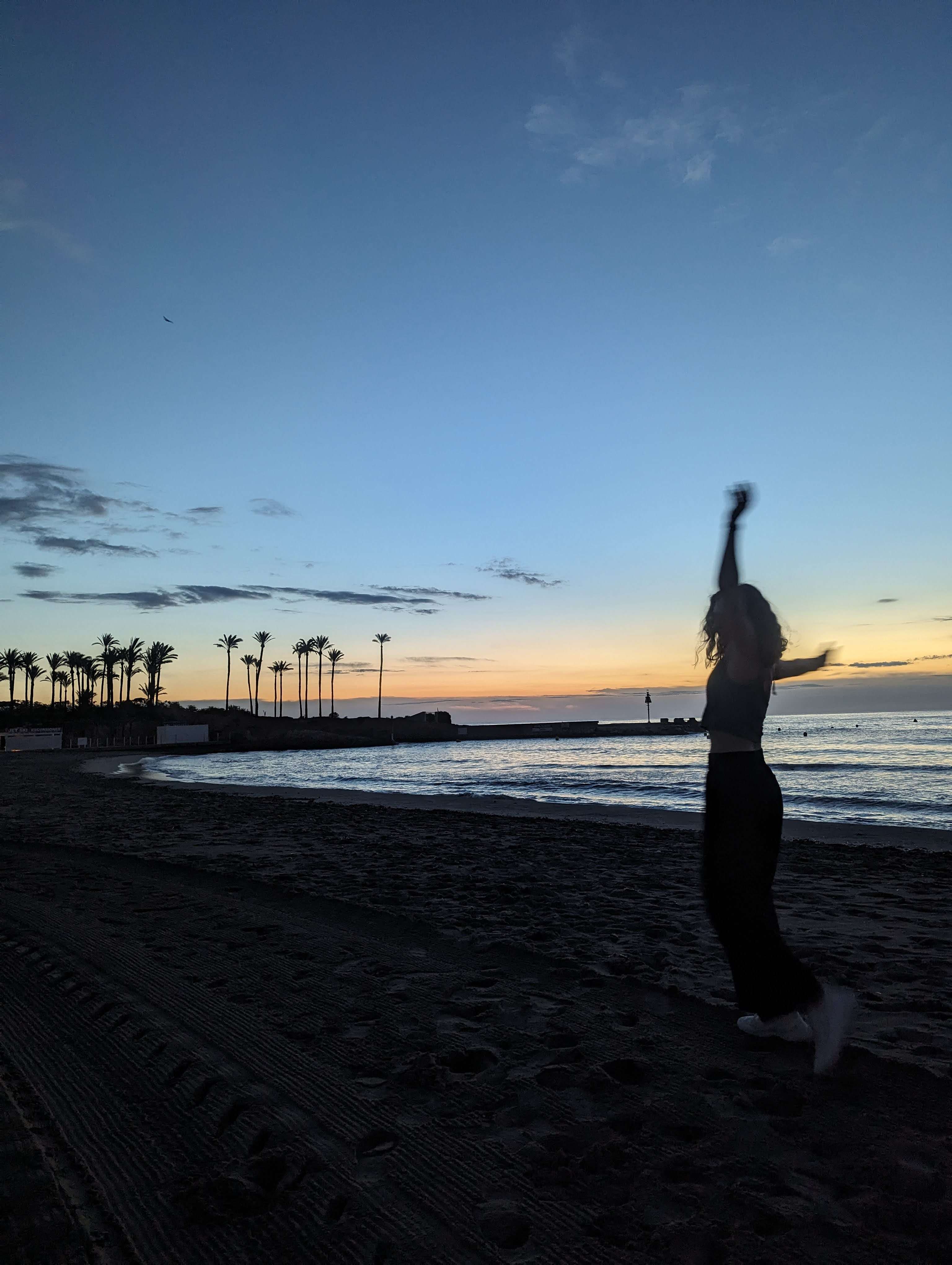 Me (Traveler Liz) spinning around in front of the sunset on the beach with the ocean and palm trees behind me.