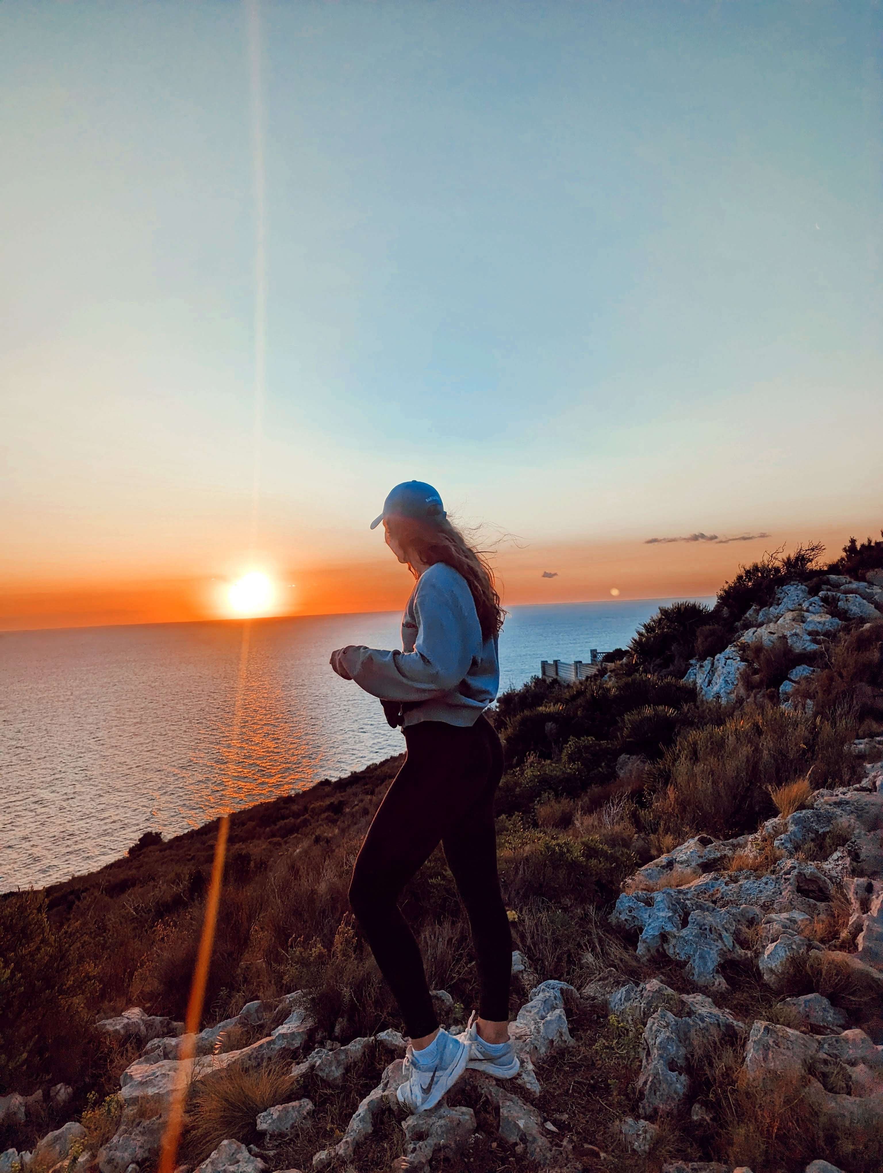 Me (Traveler Liz) standing in front of the sun watching it rise on a cliff overlooking the water.