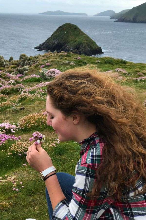 Traveler Liz smelling the flowers on a beautiful cliff in Ireland.