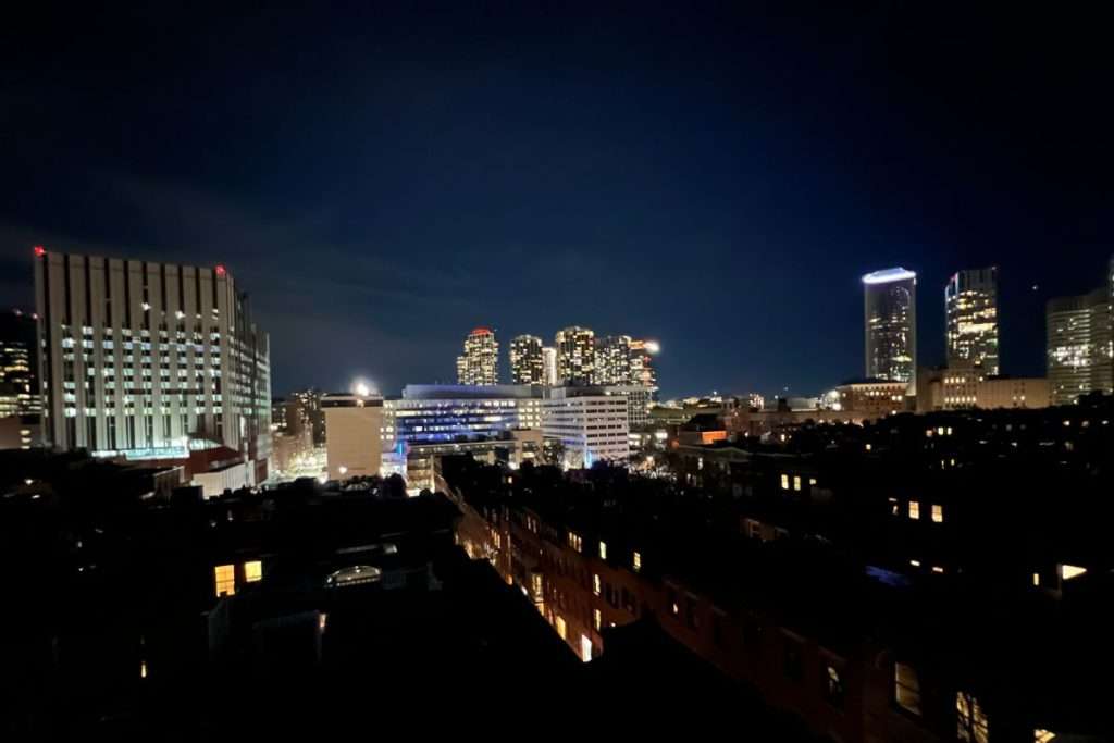 Nighttime view of Boston skyline with glowing skyscrapers and residential rooftops in the foreground