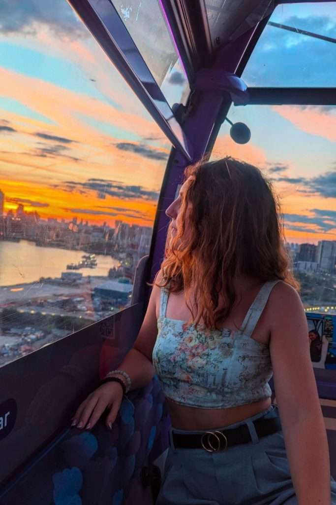 Traveler Liz admiring a vibrant sunset view of London from inside the IFS Cloud Cable Car cabin overlooking the River Thames.
