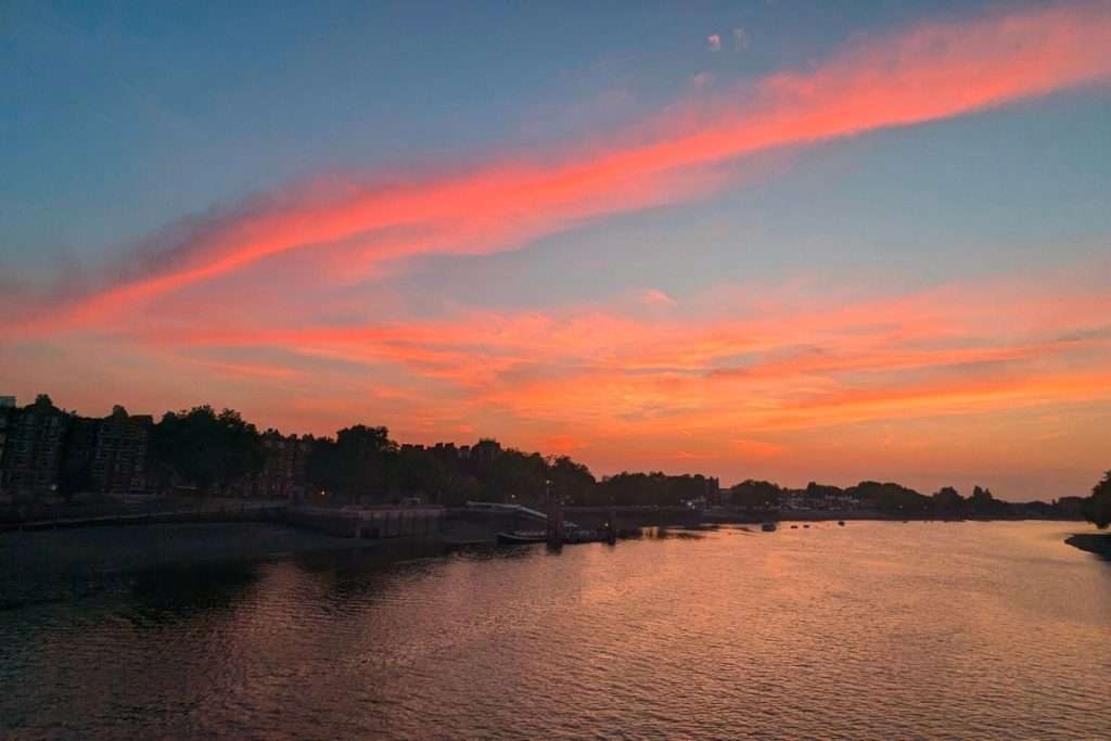Vibrant pink and orange sunset over the River Thames with reflections on the water and silhouettes of riverside buildings in London.