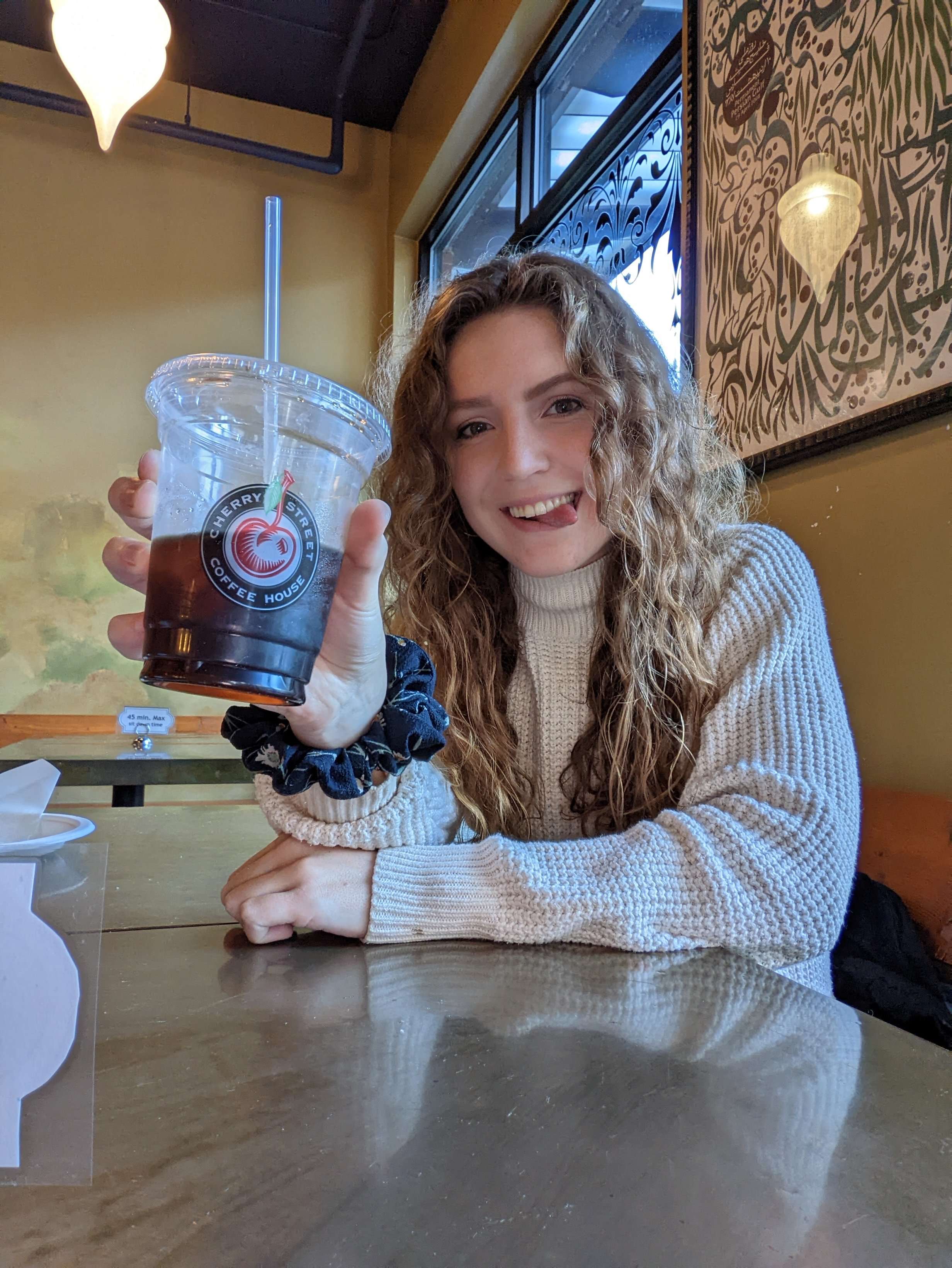 Me (Traveler Liz) sticking my tongue out and holding a coffee from Cherry St. Coffee House.