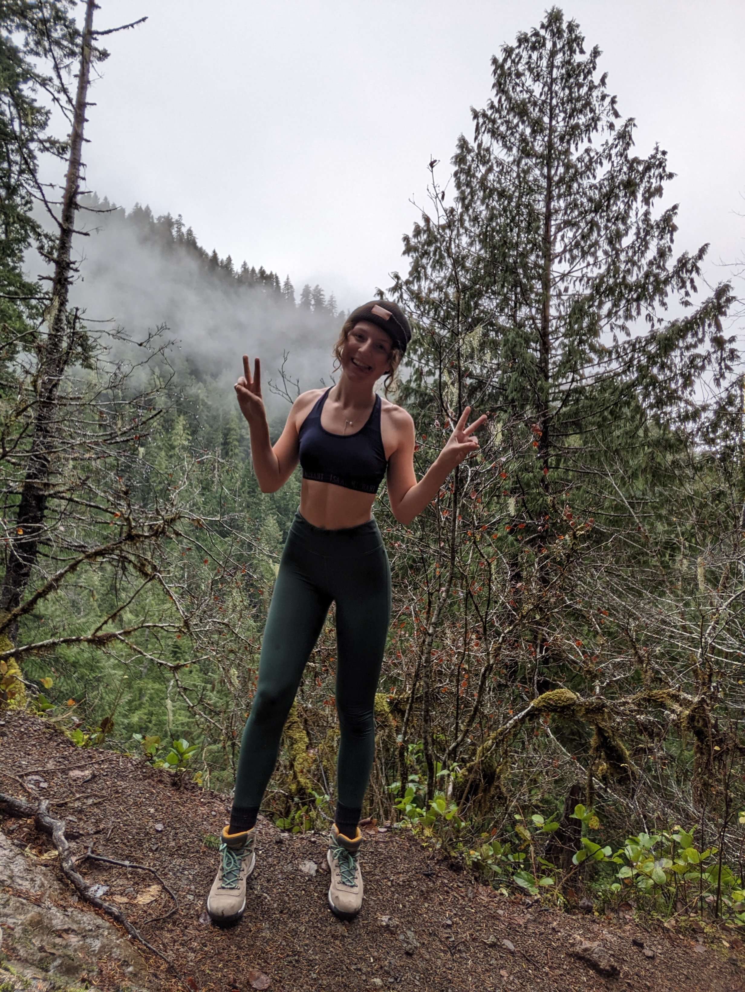 Me (Traveler Liz) posing while on The Storm King Trail at Olympic National Park with thick fog behind me.