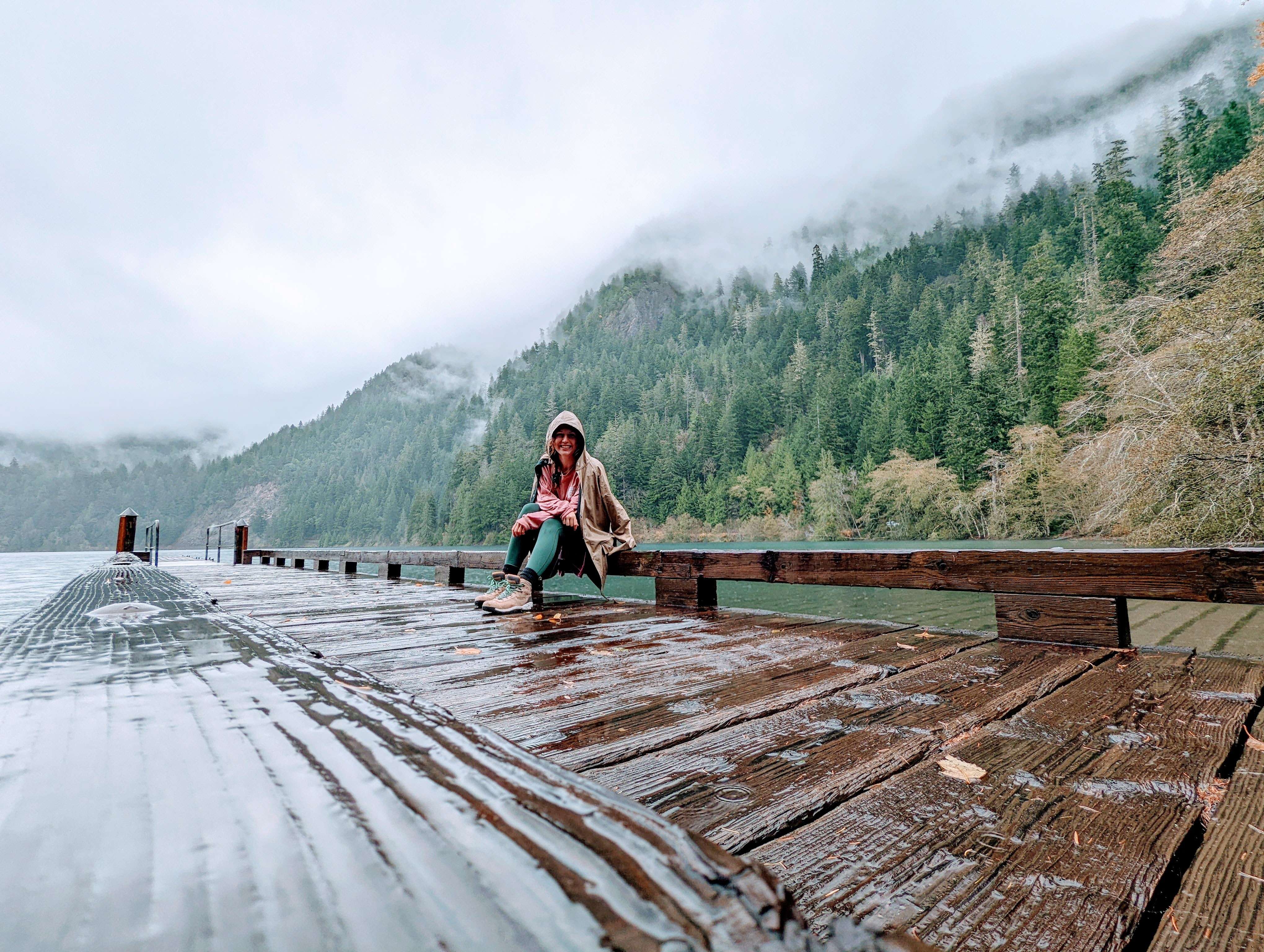 Me (Traveler Liz) sitting on a dock at Olympic National Park with the fog and trees behind me.