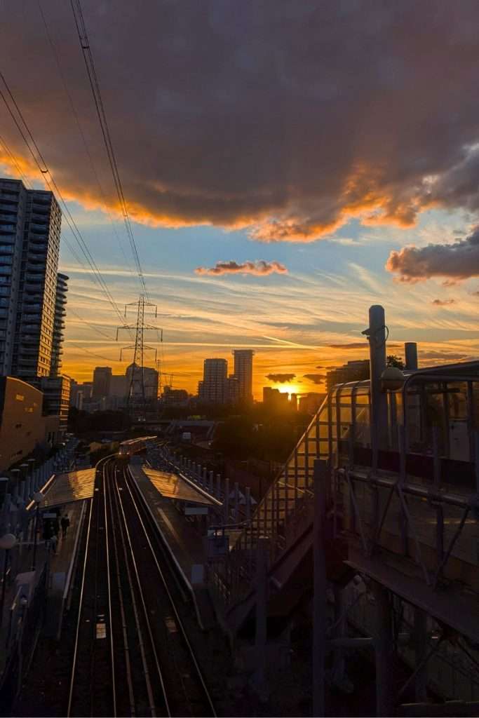 Vibrant London sunset over train tracks with skyscrapers silhouetted against an orange and blue sky.