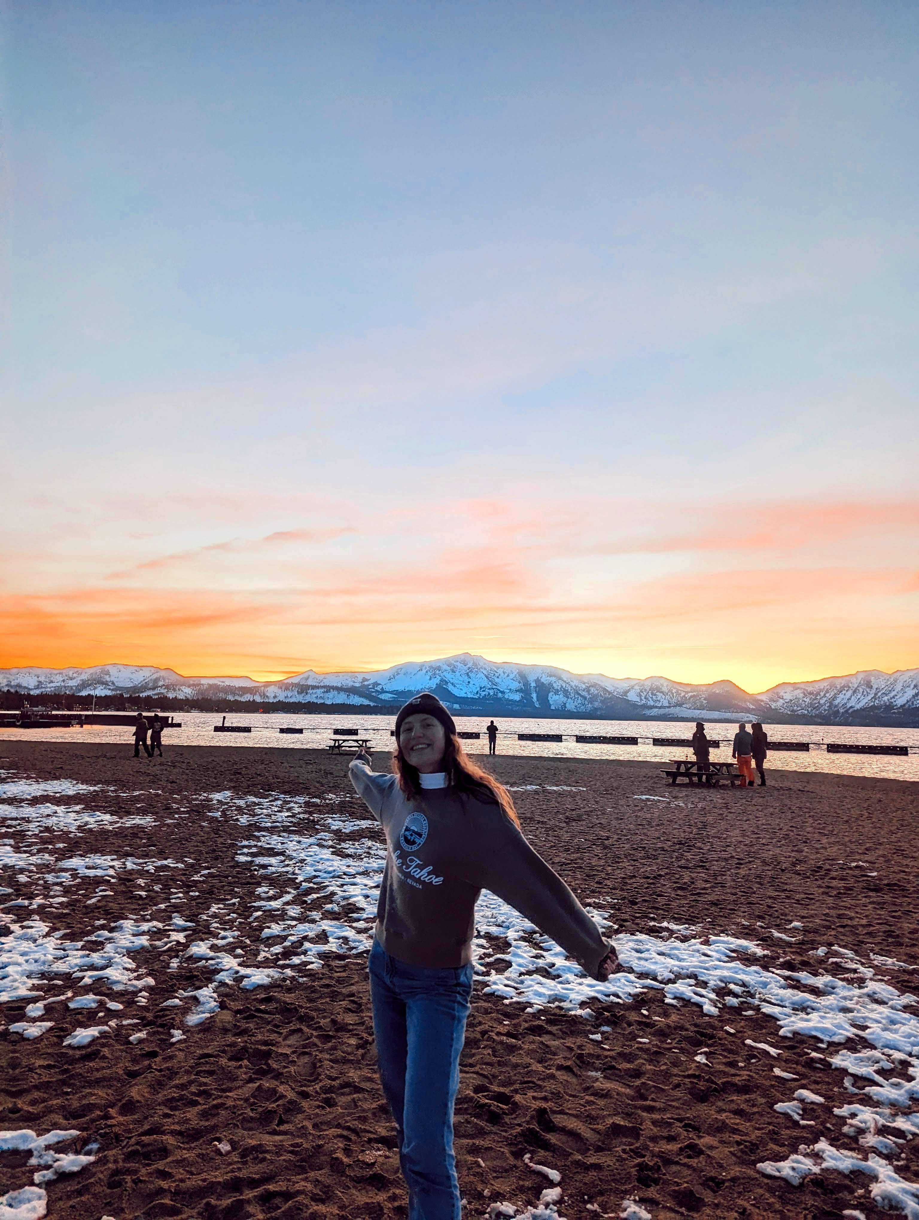 Traveler Liz in front of the sunset on the beach in South Lake Taheo