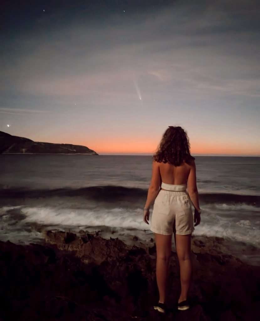 Liz in front of the ocean in with a sunset and a comet.