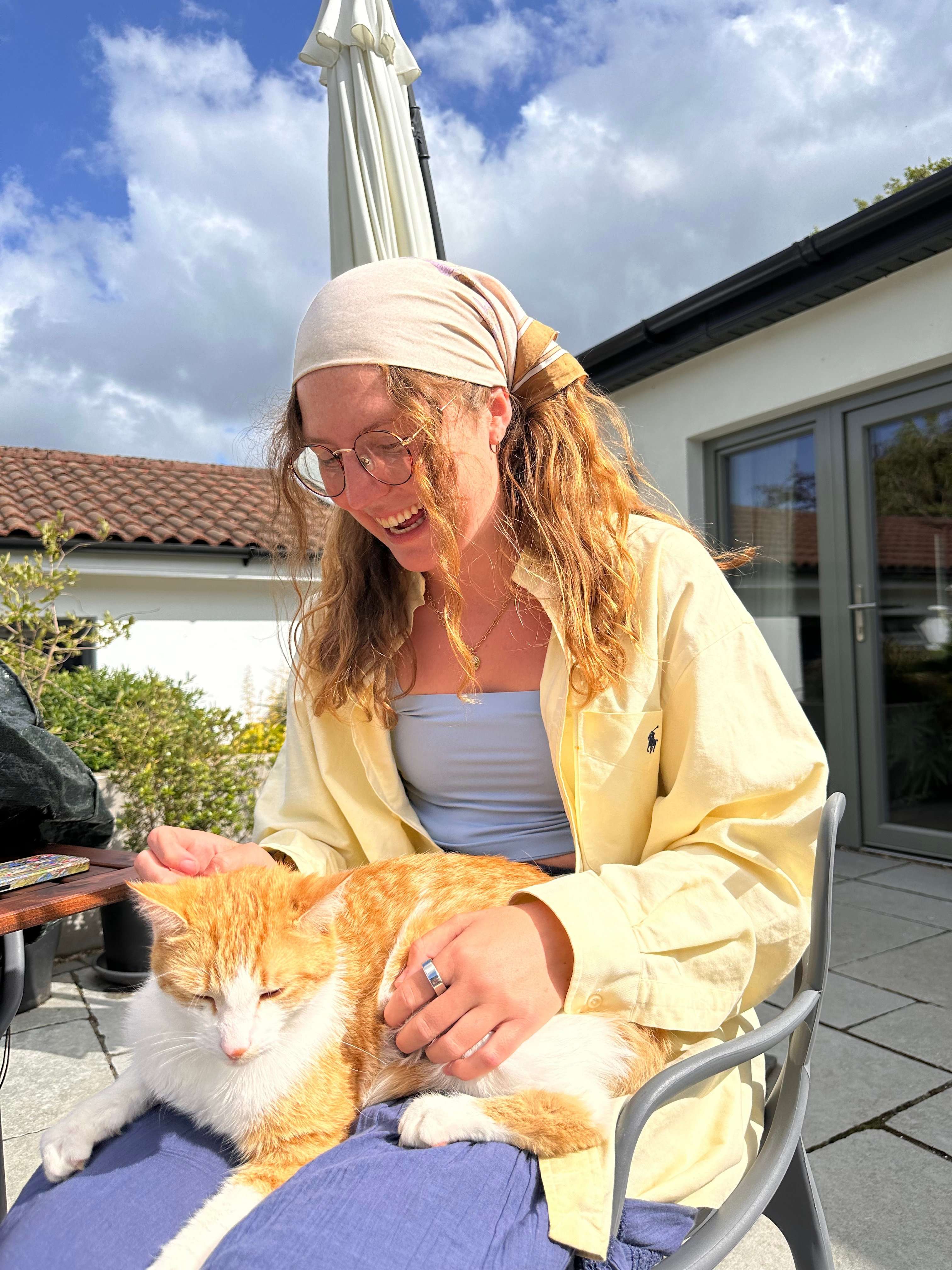 Liz sitting outside in the Irish sun with a cat on her lap.