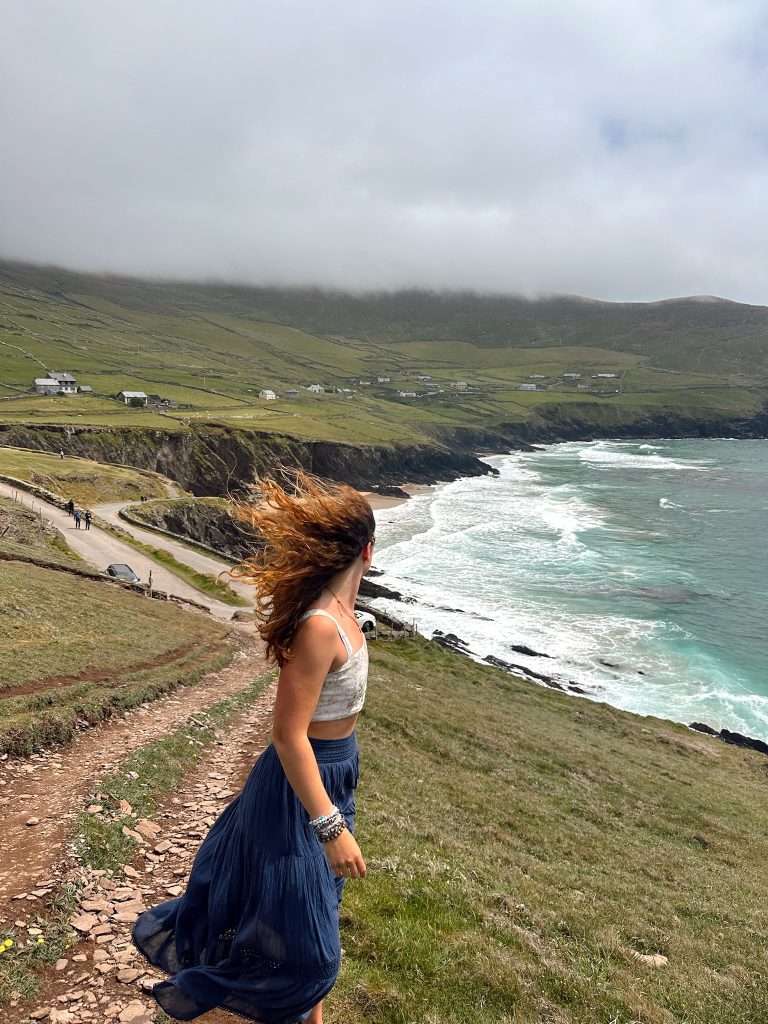 Liz looking out at Coumeenoole Beach in Ireland with hair flying in the wind.