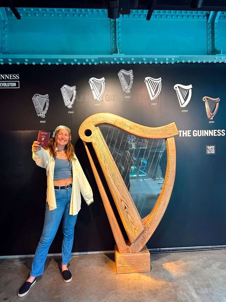 Liz holding up her Irish passport next to the famous Guinness harp in the factory.