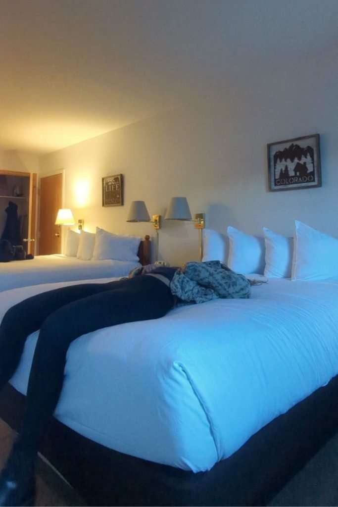 Traveler relaxing on a cozy hotel bed at the River Mountain Lodge after a ski day in Breckenridge, Colorado, comfortable lodging option for visitors staying near the slopes.