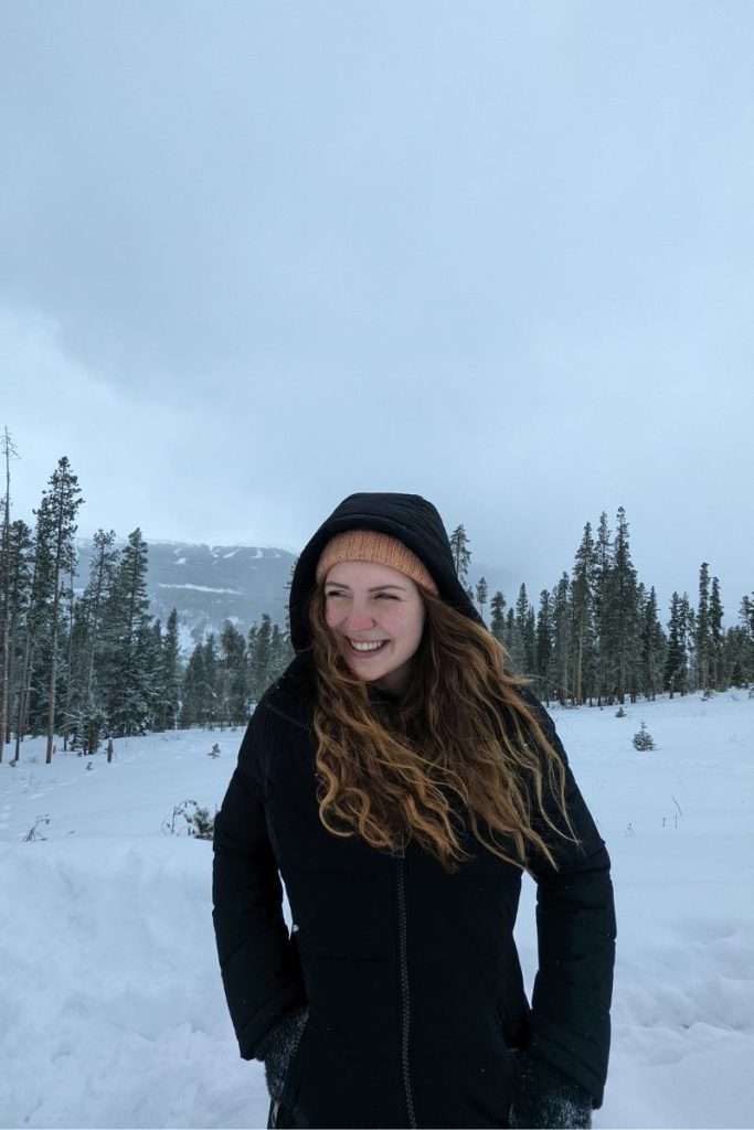 Traveler bundled up in a warm winter coat and beanie, standing in the snowy Colorado mountains, dressed for cold weather on a ski trip.