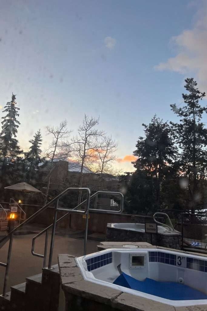 Outdoor hot tubs at a Breckenridge hotel surrounded by pine trees and mountain views at sunset, relaxing après-ski spot for guests staying in Colorado.