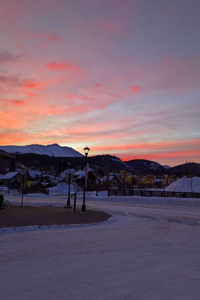 Colorful winter sunrise over Breckenridge, Colorado, with snow-covered streets, glowing mountains, and twinkling lights, a peaceful start to the day in this top USA ski town.