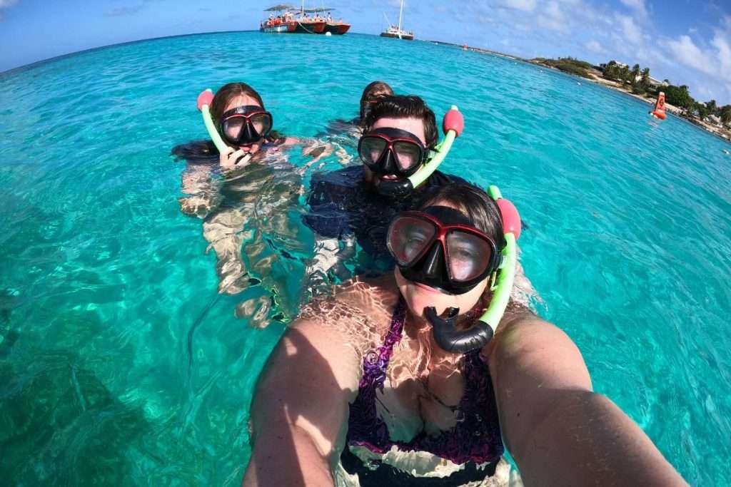 Group of snorkelers floating in bright turquoise water during a guided snorkeling tour in Aruba, with boats and a tropical coastline in the background.