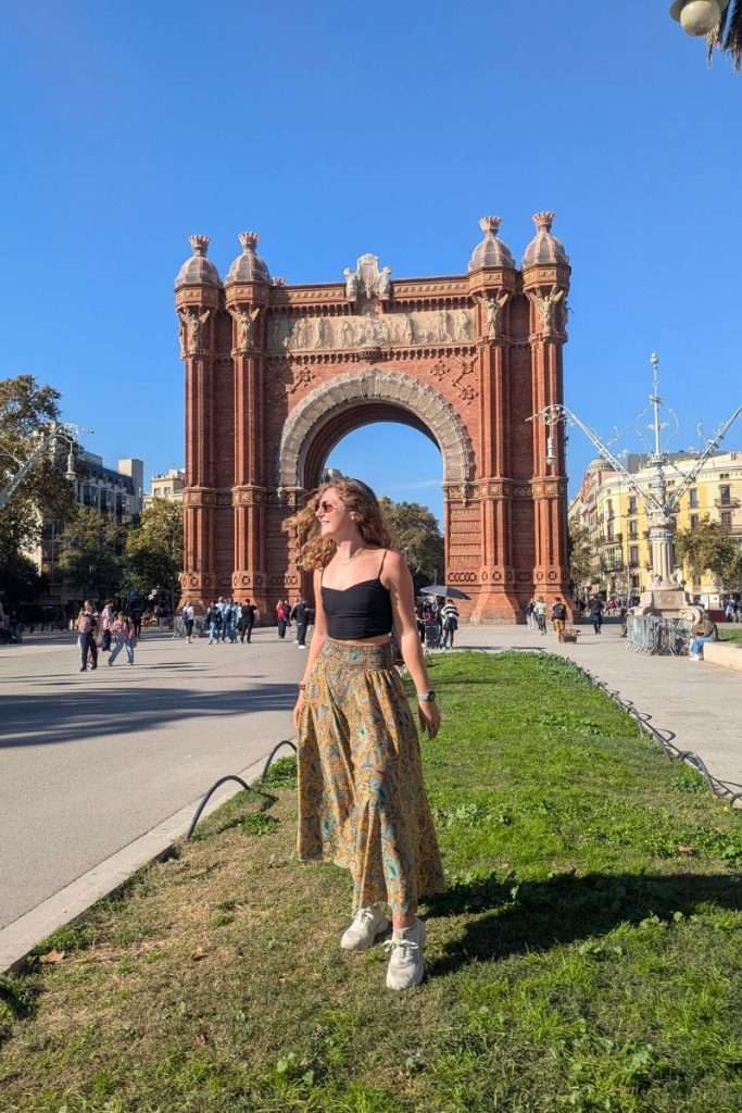 Traveler Liz standing on a sunny day in front of the Arc de Triomf in Barcelona, with people walking through the plaza behind her.