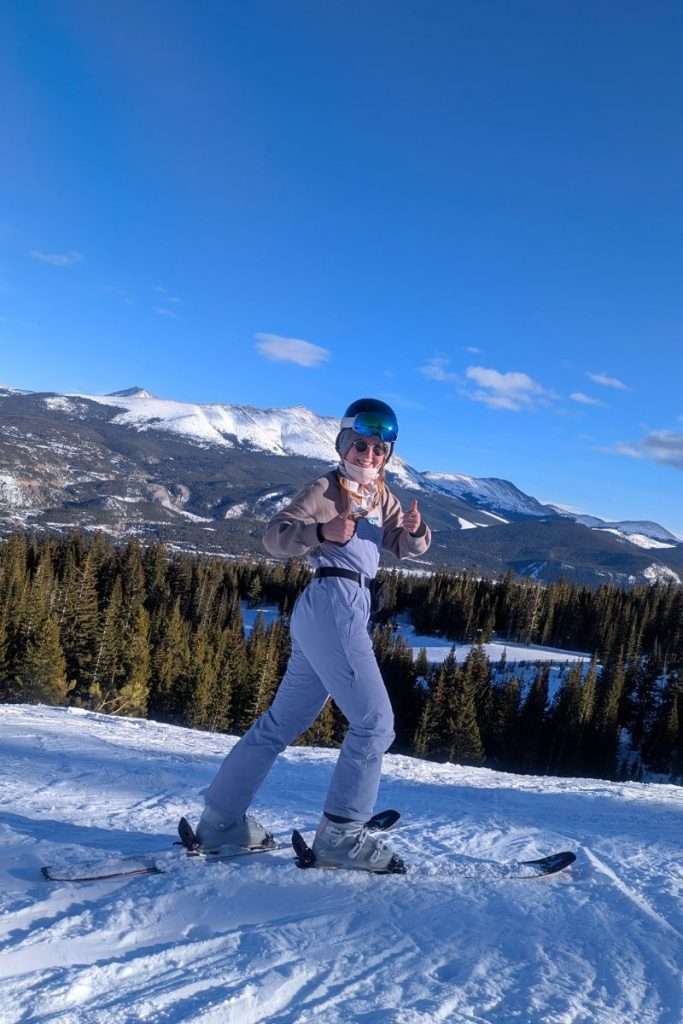 Woman skiing on a sunny day in Breckenridge, Colorado, wearing a light snow suit, helmet, and goggles, showing what to wear for a Colorado ski trip.
