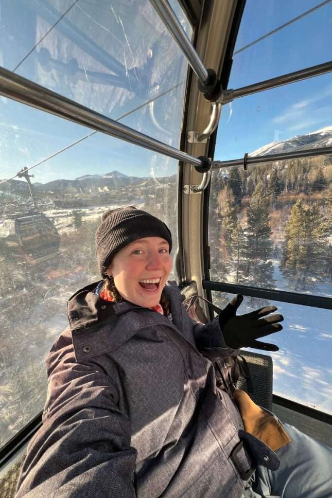 Woman riding a ski gondola in Colorado wearing a winter jacket, gloves, and beanie, dressed warmly for a day on the slopes and a Colorado ski trip.