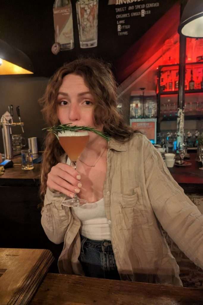 Liz holding a drink with rosemary on top at Het Concerthuis