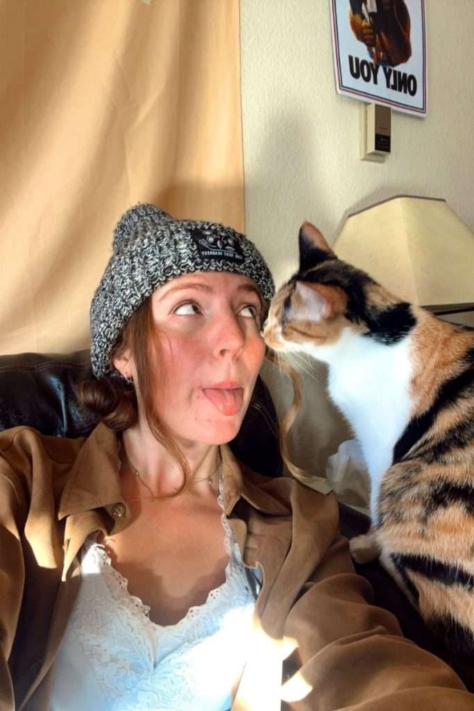 A cozy indoor moment showing a woman in casual clothing interacting playfully with a calico cat beside her.