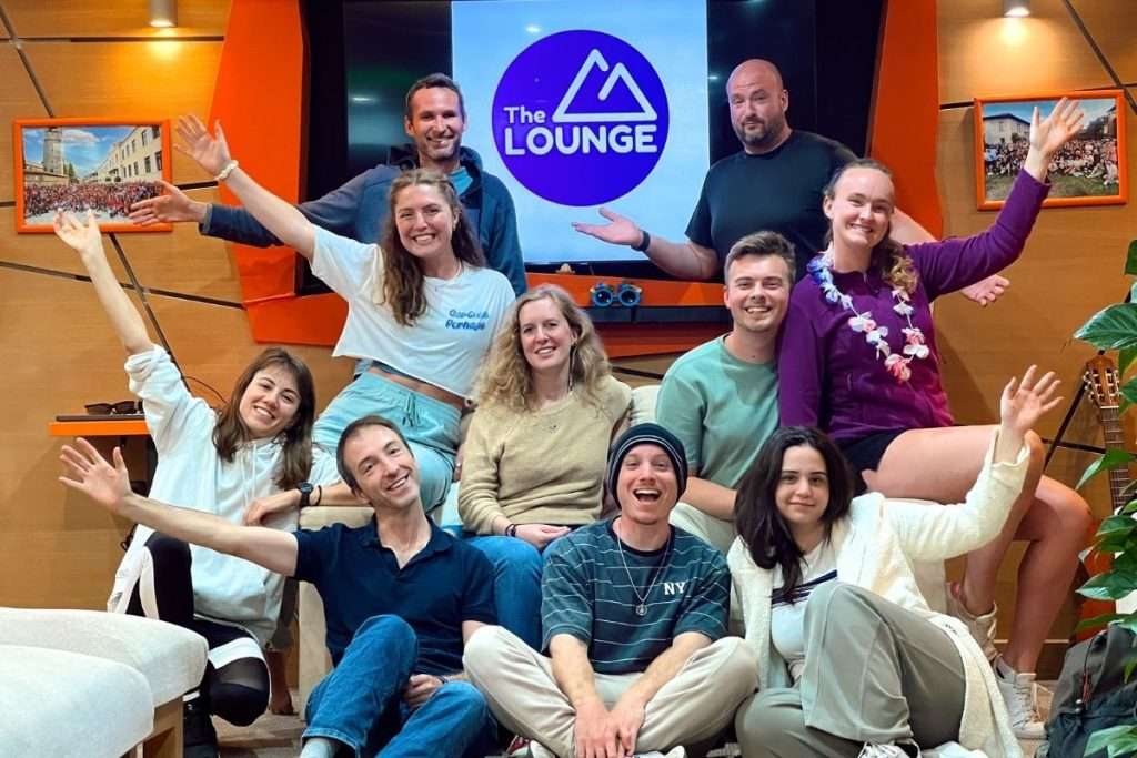 A diverse group of people gathered in a lounge-style room, smiling and posing together with raised arms, capturing a sense of community and connection.