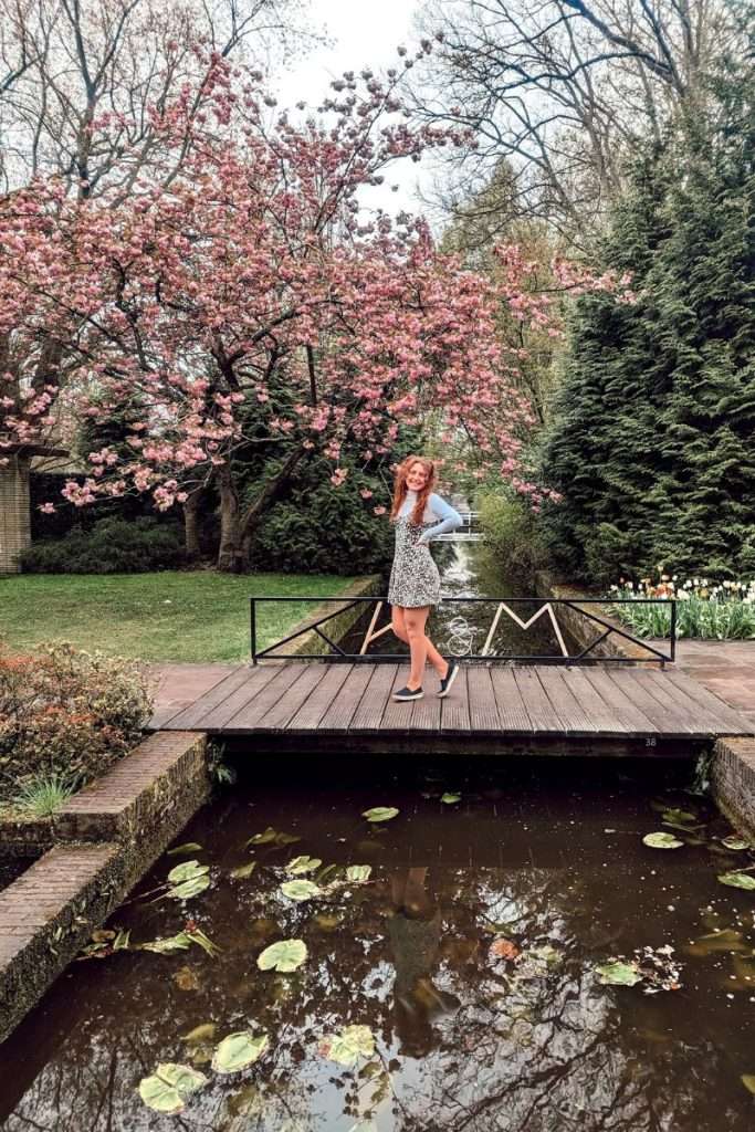 Liz posing on a bridge in Keukenhof surrounded by greenery and flowers.
