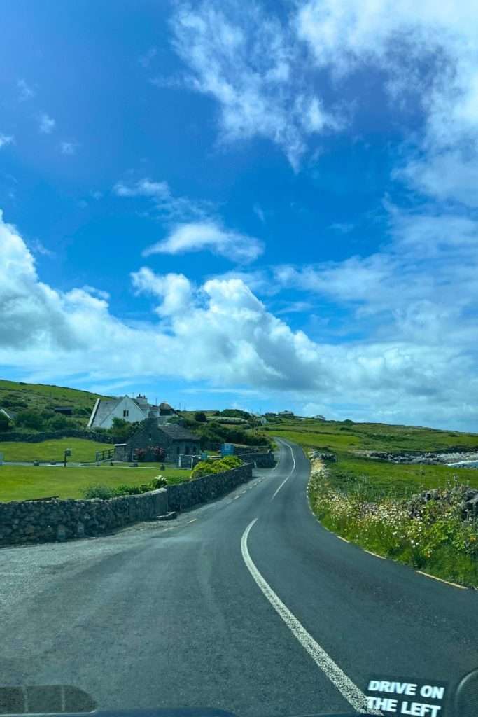 A narrow road in Ireland in a rural area with the "drive on the left" sign showing in the corner.