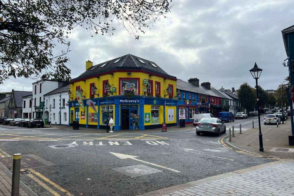 An intersection in Ireland with a colorful pub in the middle and cars along the streets.