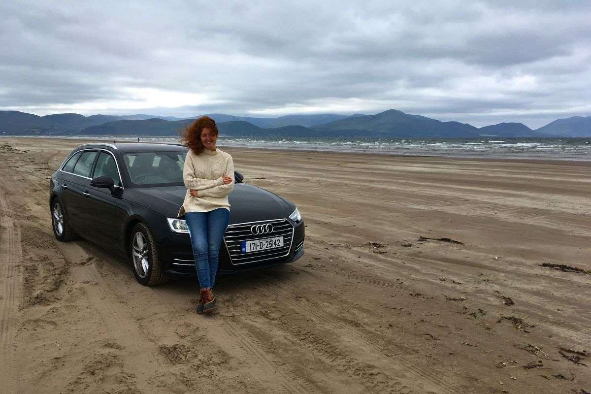 Woman standing by rental car on a beach in Ireland during a Galway day trip with mountains in the background