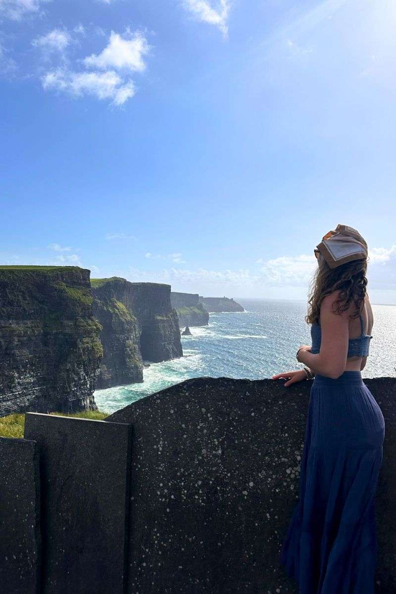 View of Liz standing next to the Cliffs of Moher on a beautiful sunny day in Ireland.